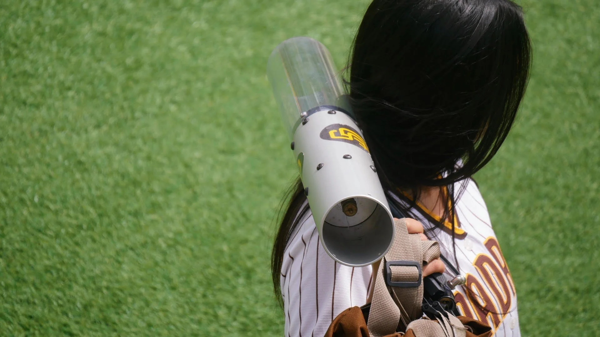 A person with long dark hair wearing a baseball jersey and holding a megaphone on a grassy field.