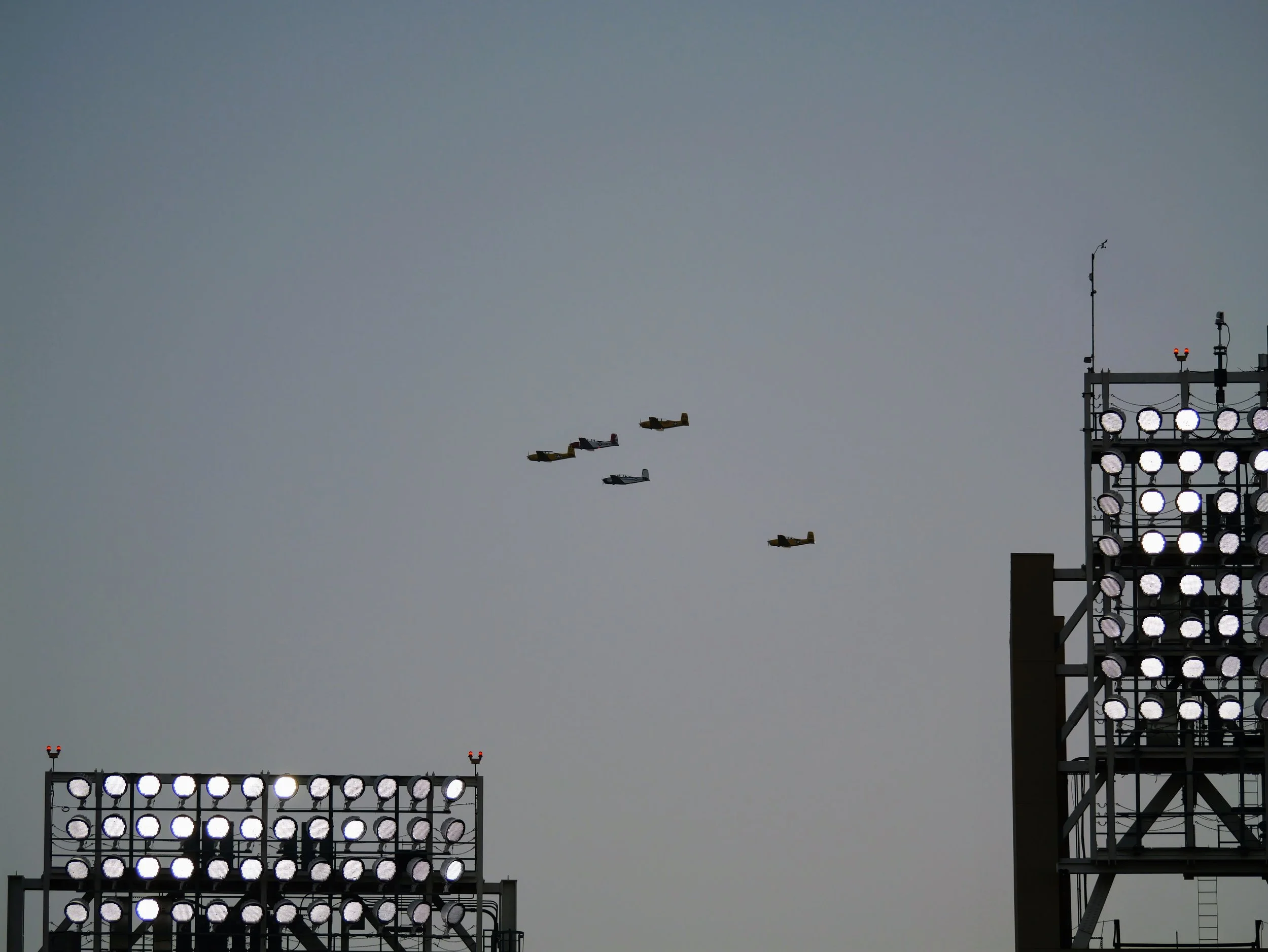A small aircraft flying past a large power tower with multiple lights and antennas during dusk.
