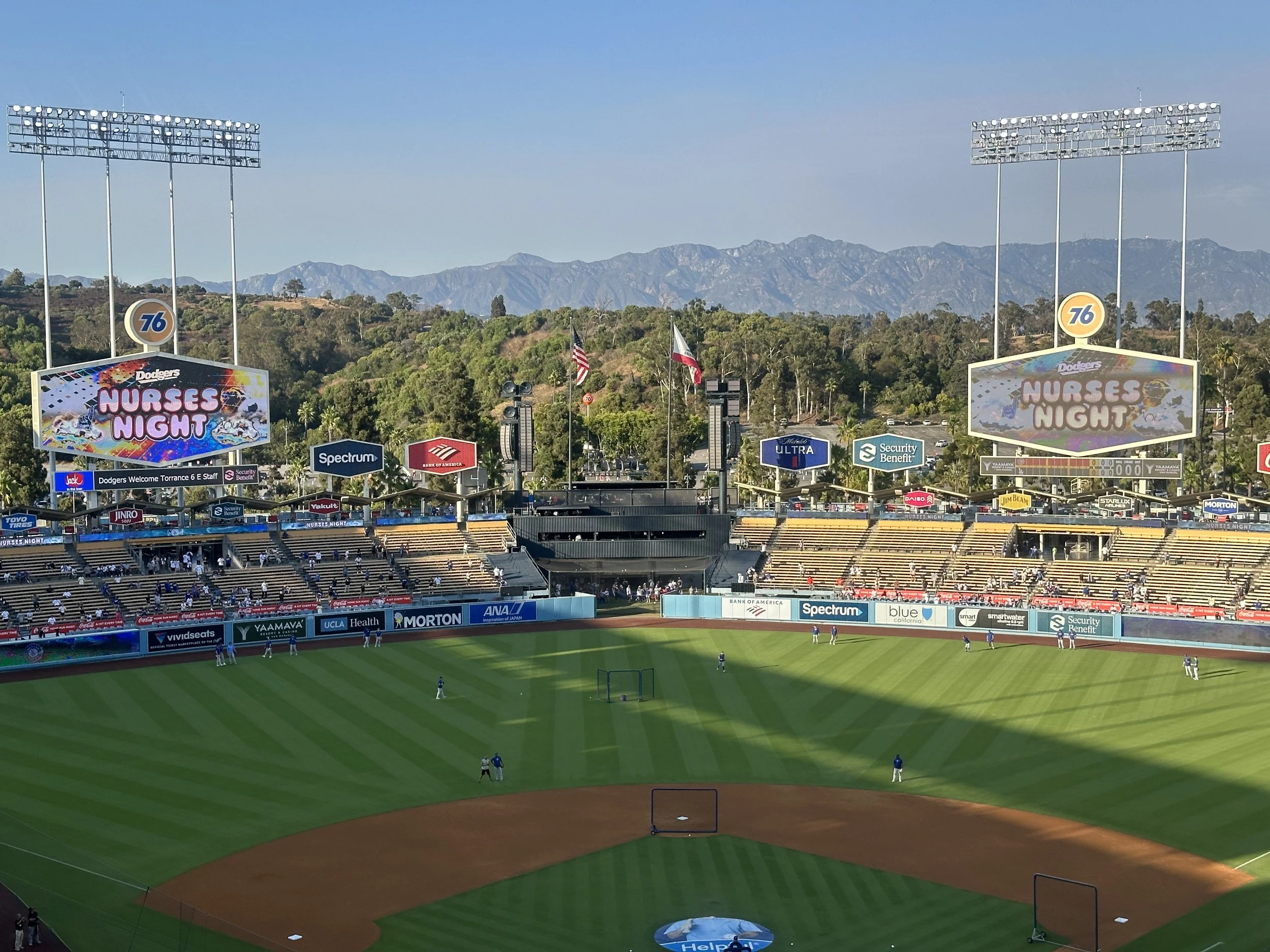 View of a baseball stadium with players warming up on the field, spectators in the stands, and mountains in the background, during a Dodgers' game night event.