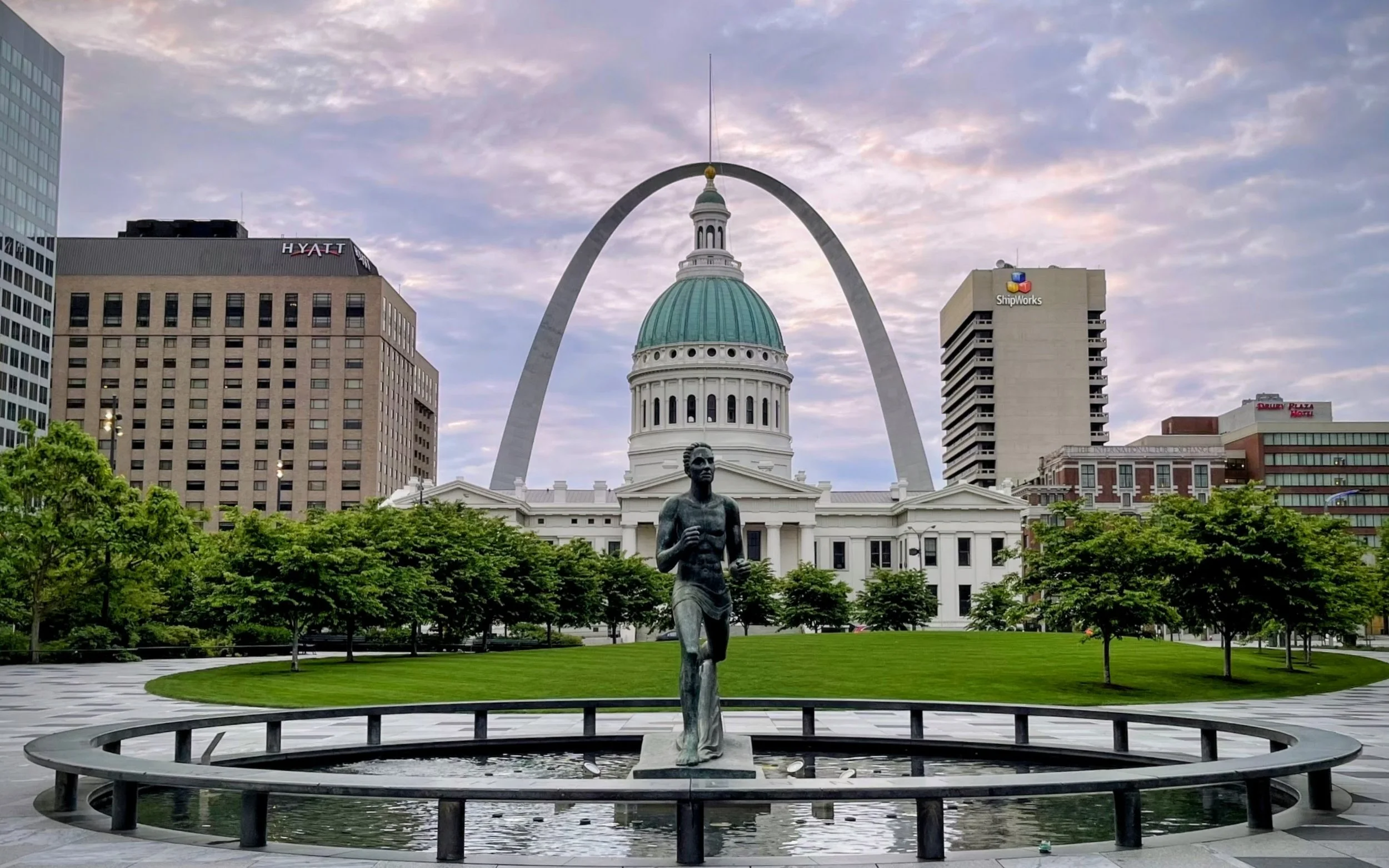 Downtown St. Louis with the Gateway Arch, the Old Courthouse, and a statue of a running man in a fountain.