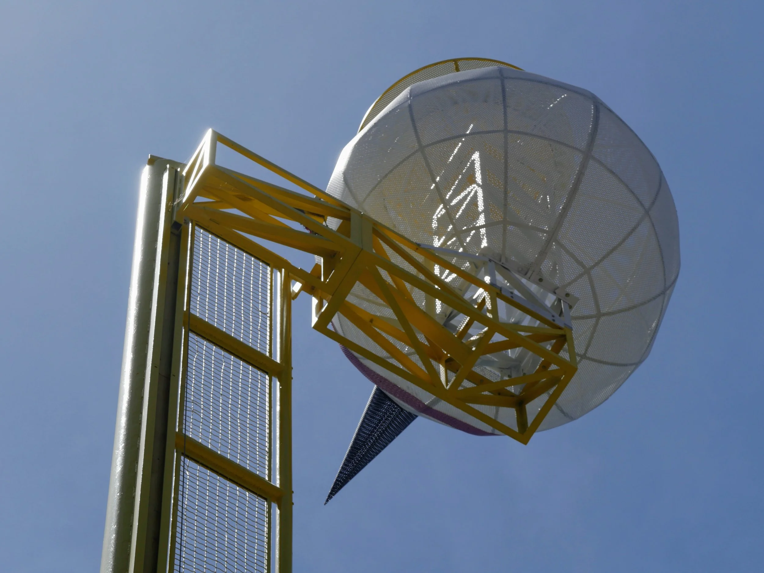 Close-up of a communication or radar tower with a large satellite dish and yellow structural supports against a clear blue sky.