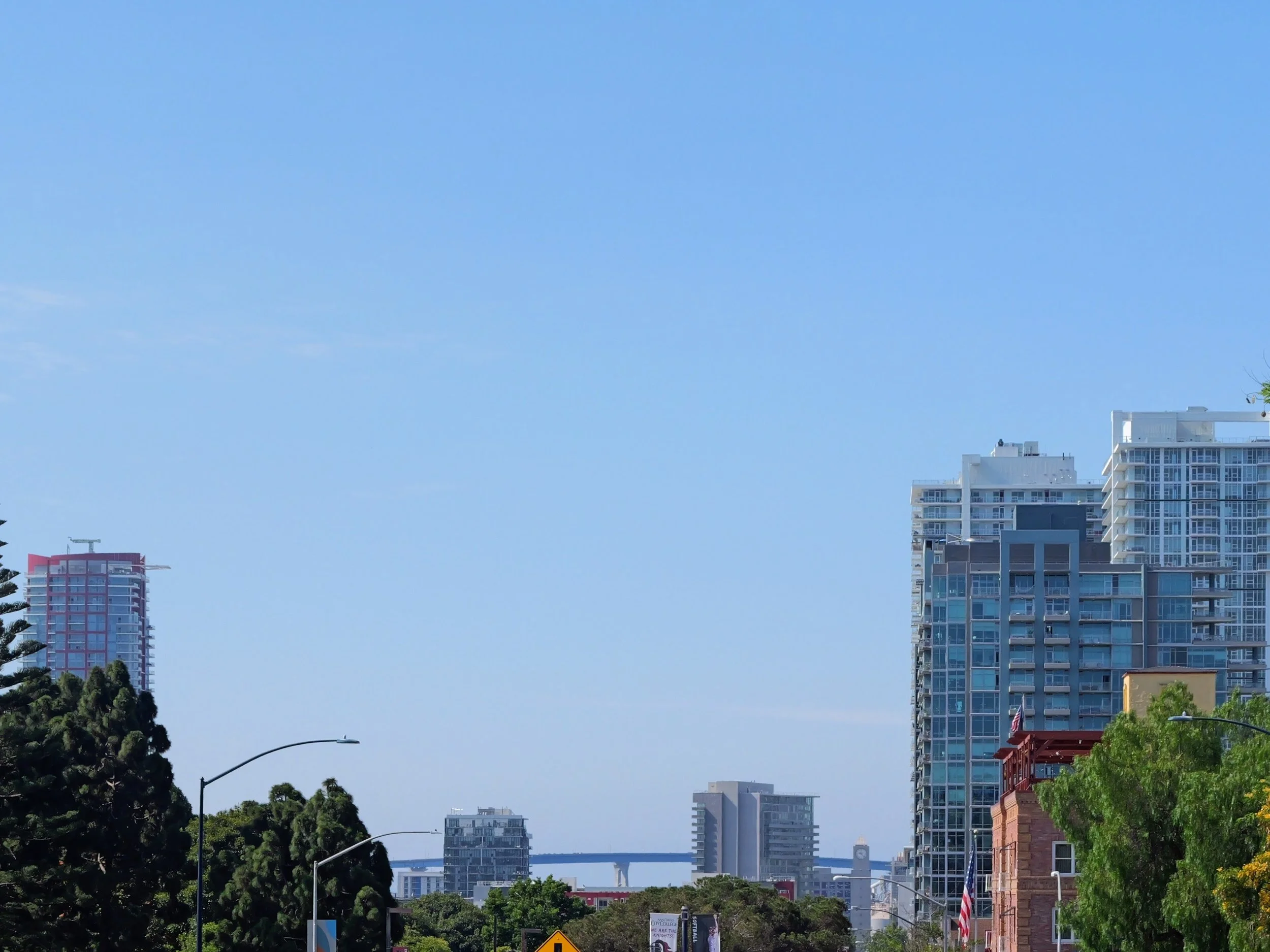 Cityscape with high-rise buildings, trees, and a clear blue sky.