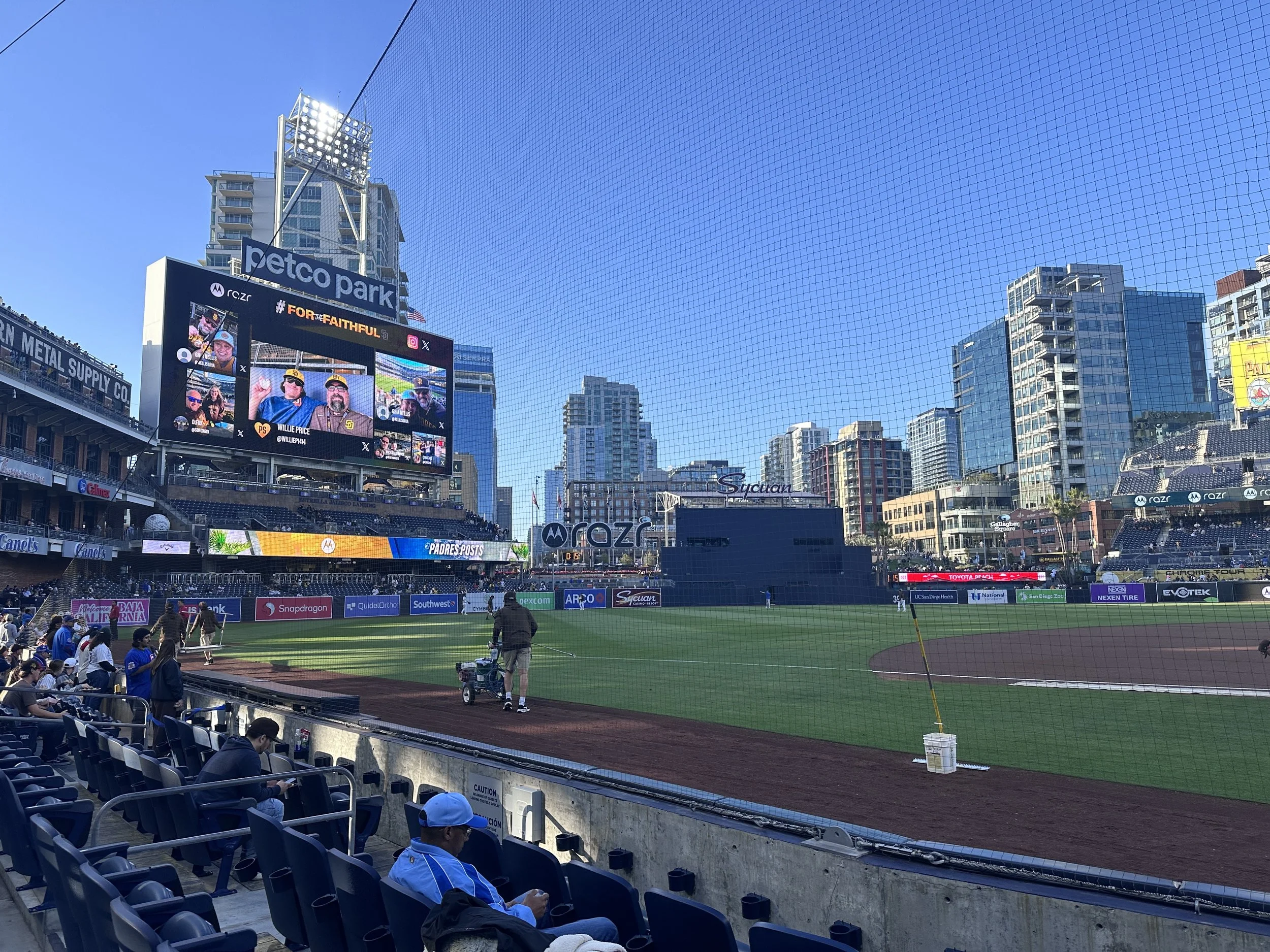 View of Petco Park baseball stadium with a large electronic scoreboard displaying fans and players, surrounded by modern high-rise buildings on a clear day.
