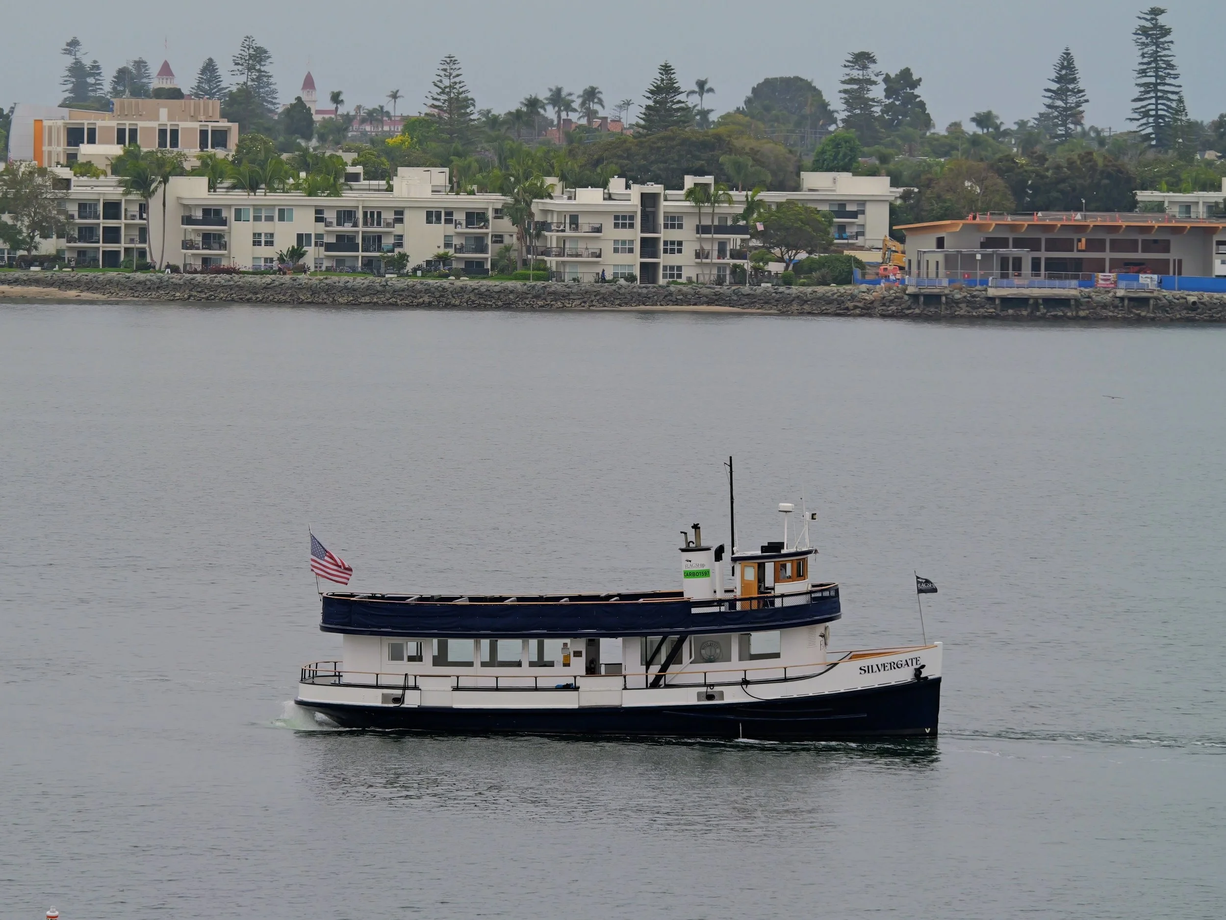 A boat named 'Silvergate' sailing on a body of water with buildings and trees on the shoreline in the background.