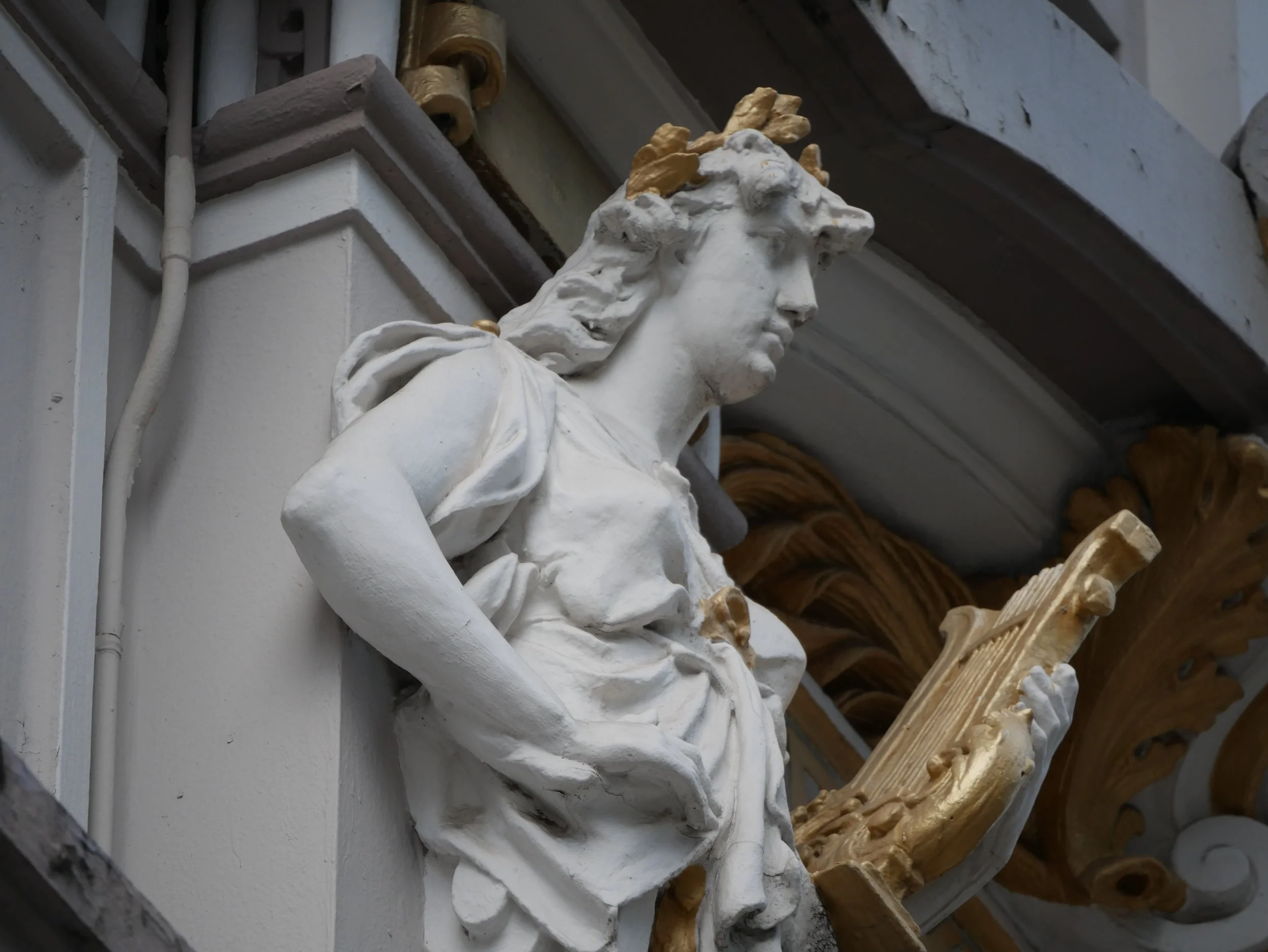 Close-up view of a decorative architectural sculpture of a woman's face with flowing hair, likely part of a building's ornamentation, with other decorative elements and intricate details visible around.