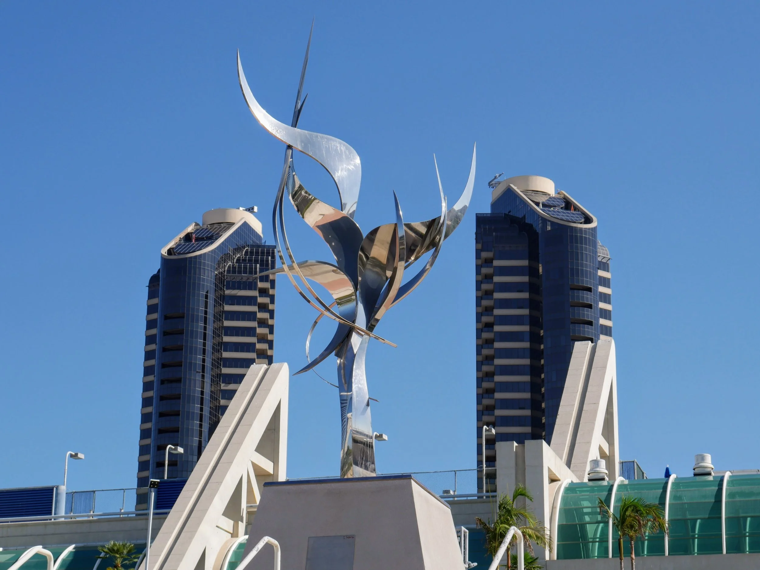 Modern high-rise building with a metallic sculpture in front, under a clear blue sky.