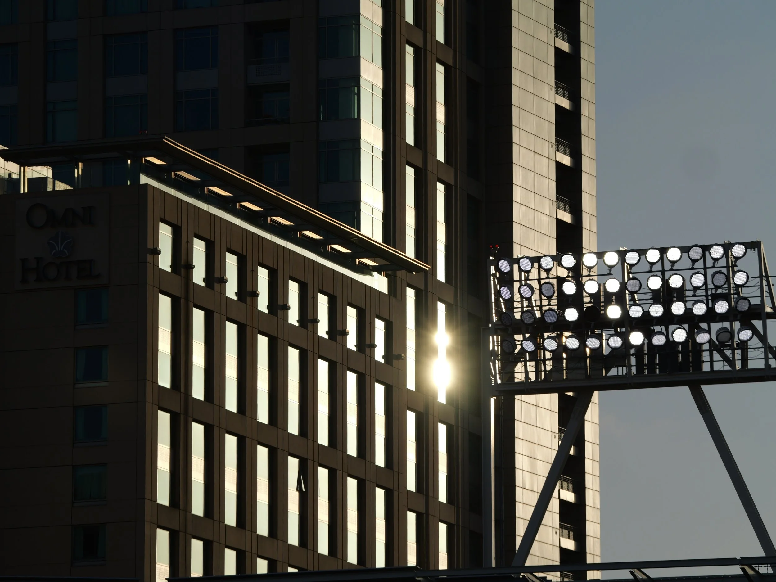 A tall modern building with glass windows, reflecting sunlight, and a clear sky background. There is a structure with circular lights in front of the building.