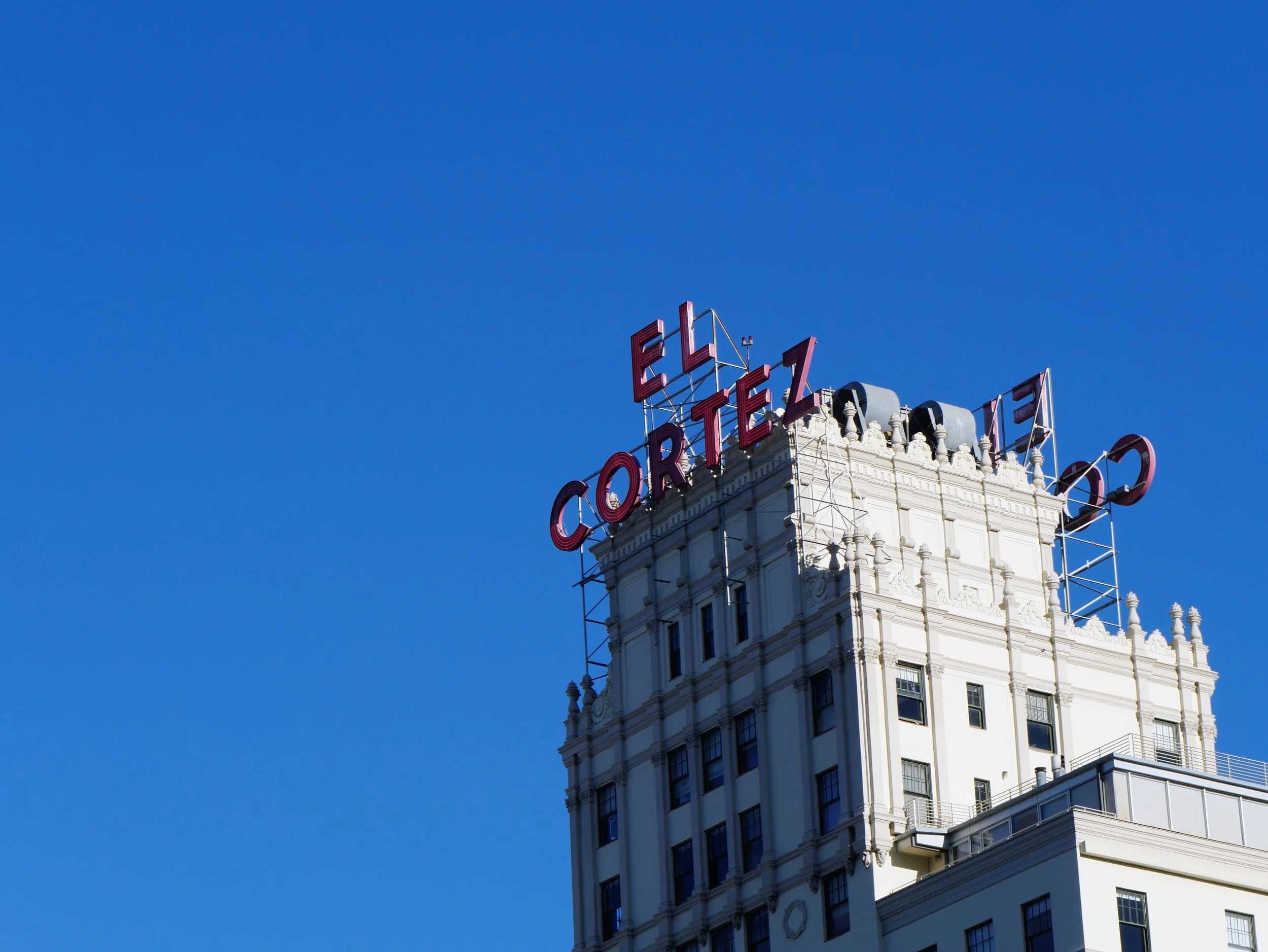 A tall white building with decorative architecture and a red neon sign reading 'EL' and 'ORTEL' on top, set against a clear blue sky.