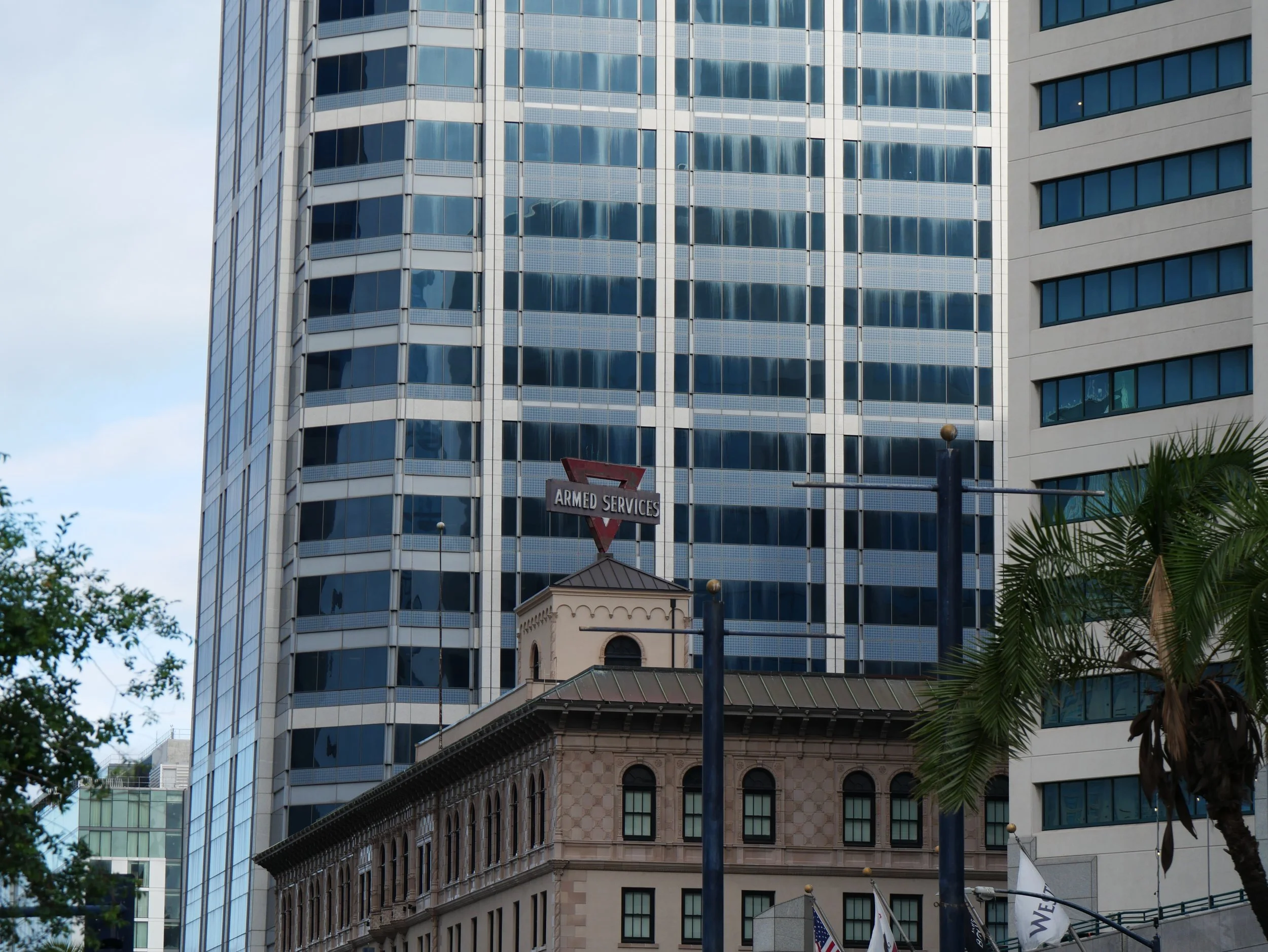 Tall office buildings with glass and stone facades in an urban setting, with trees and flags in the foreground.
