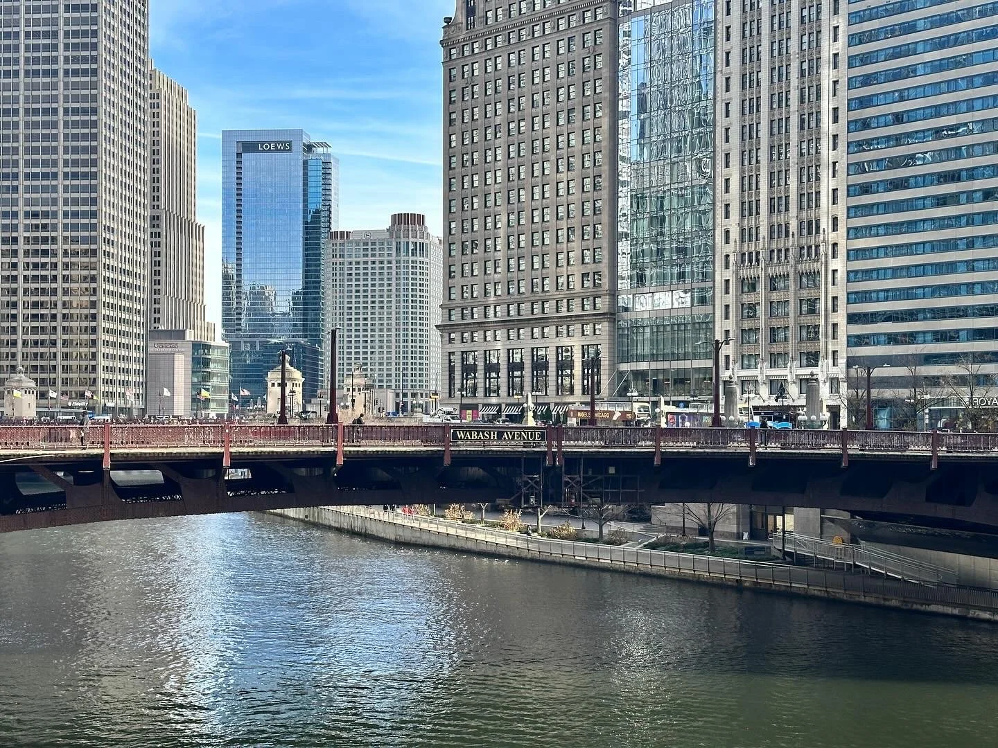 Cityscape of high-rise buildings along a river with a bridge across it, under a clear blue sky.