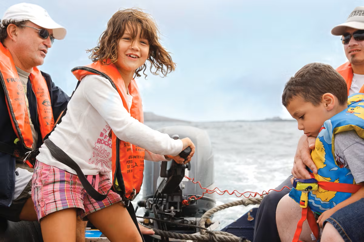 Kids enjoying driving a zodiac aboard Lindblad expeditions ship at Galapagos, on its Explorers in Training program