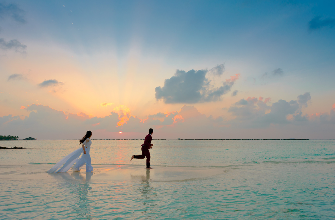 Romantic getaway showing a just married couple running in shallow ocean water during sunset
