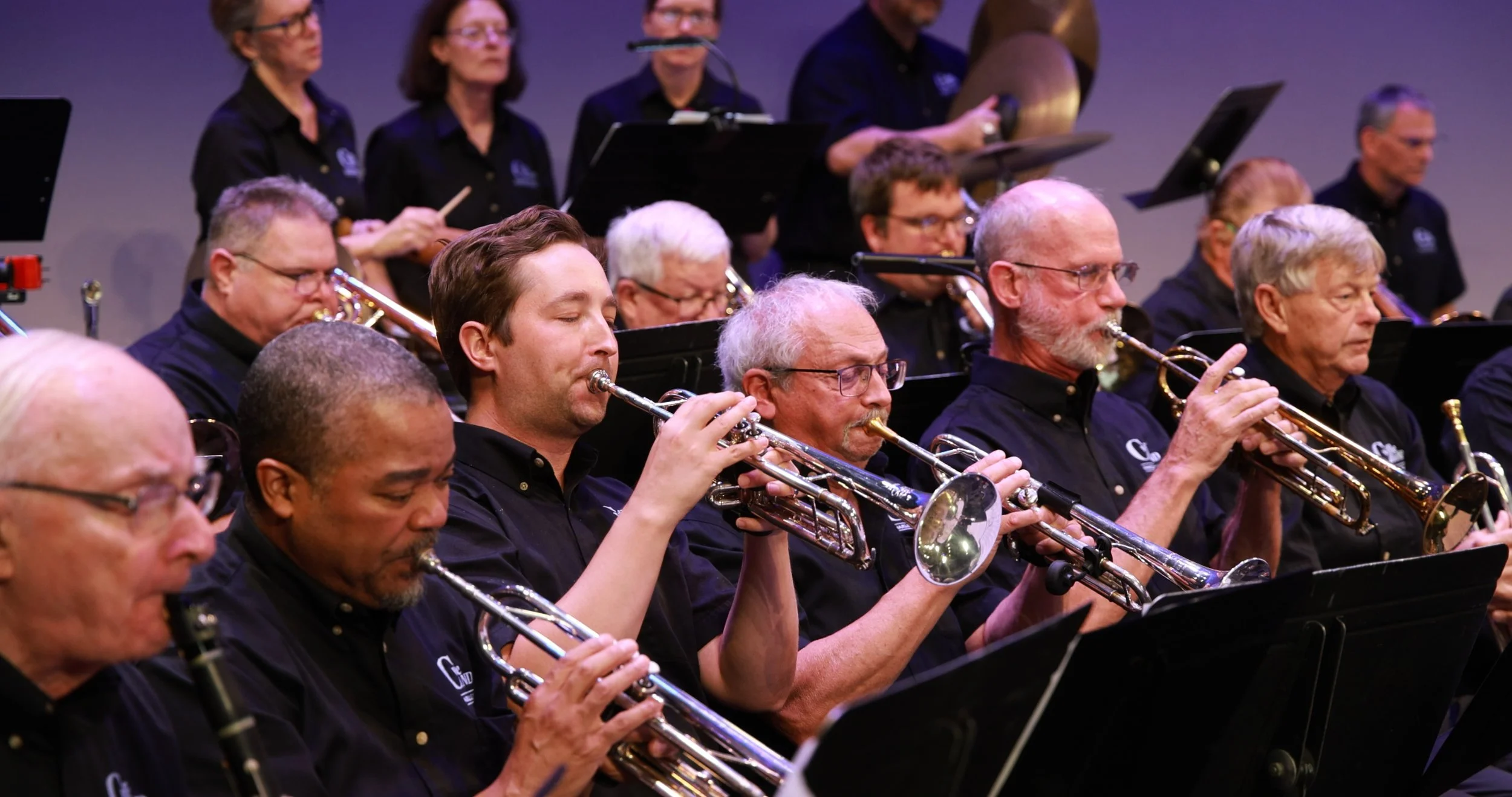 A large group of musicians playing brass instruments, including trumpets, during an orchestra performance.