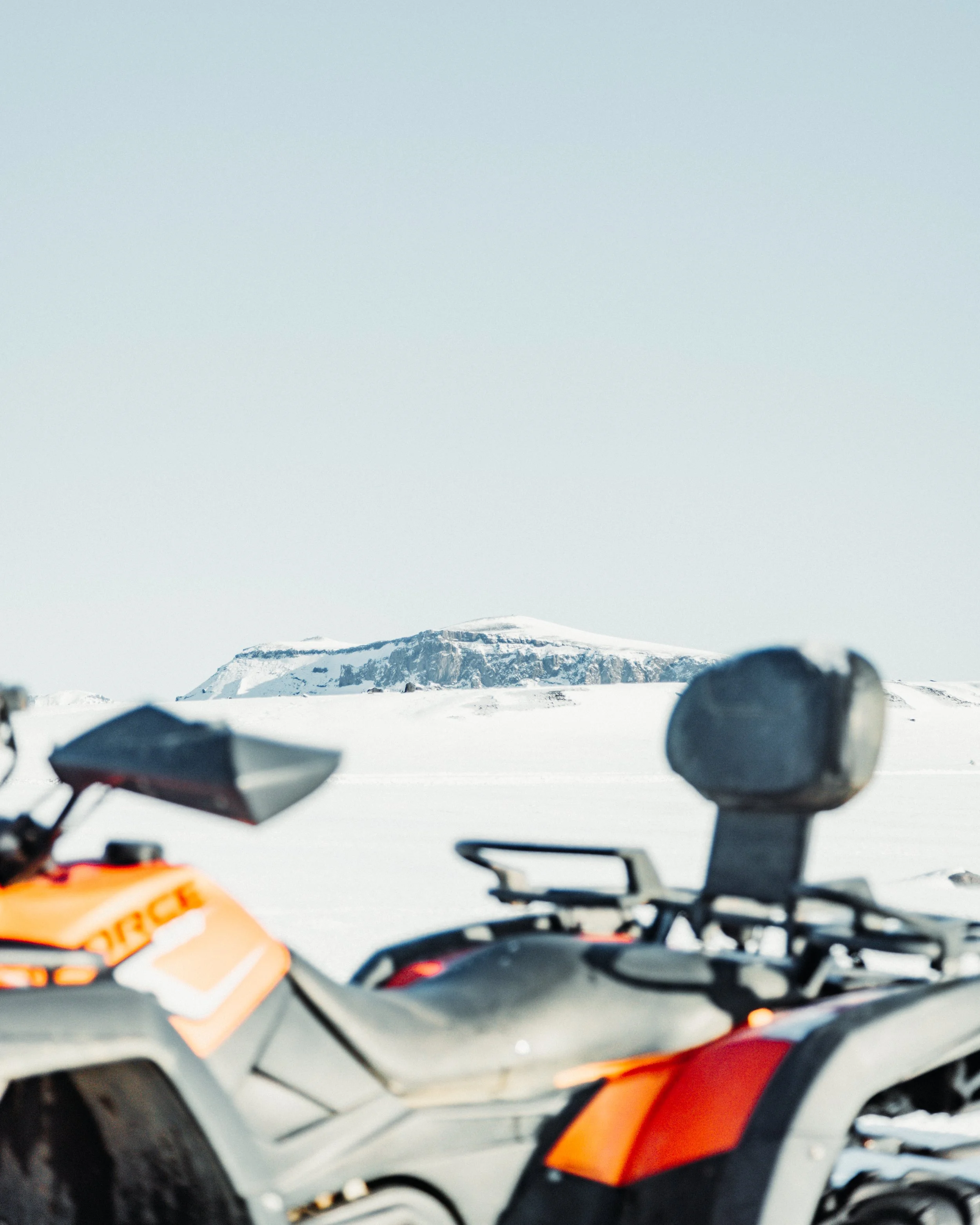 Snow-covered landscape with a mountain in the background and an orange and black adventure motorcycle in the foreground.