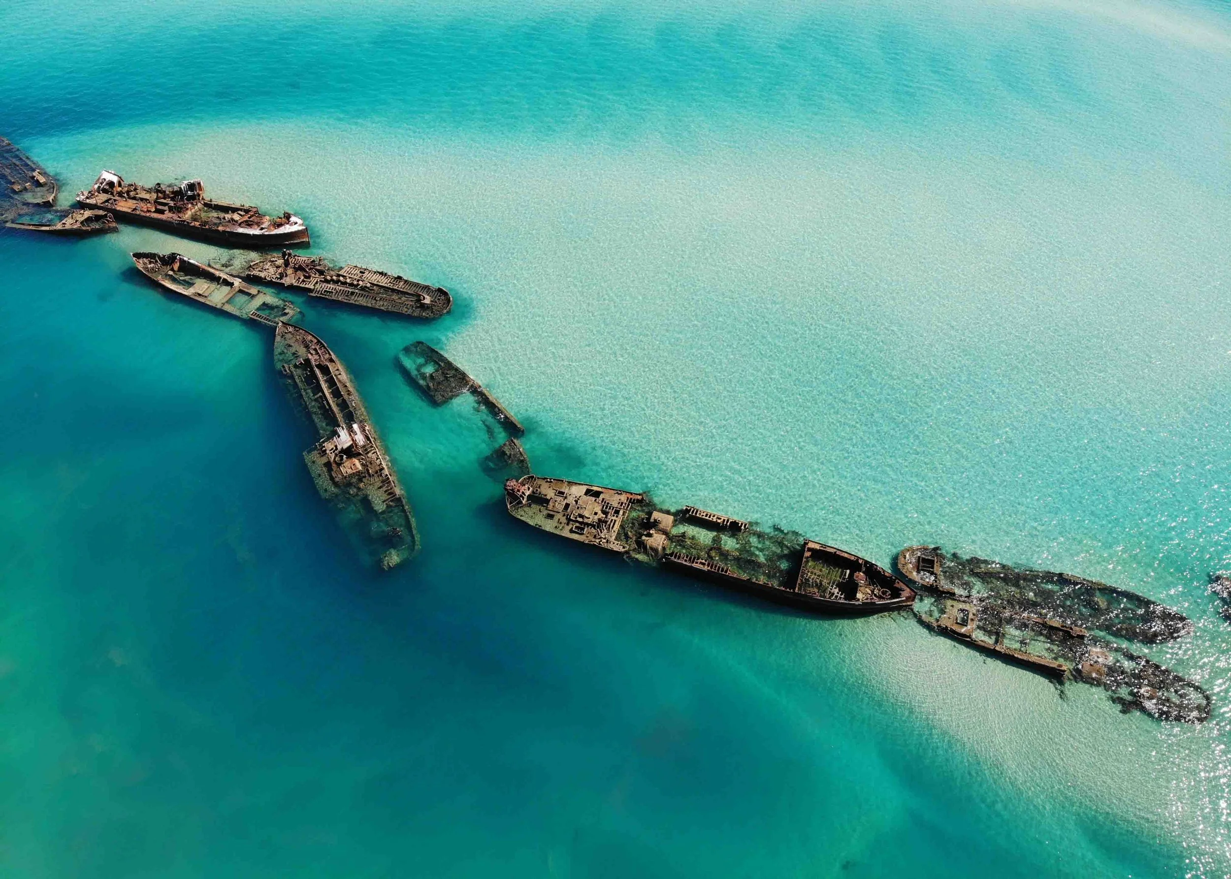 Aerial view of shipwrecks partially submerged in turquoise water.
