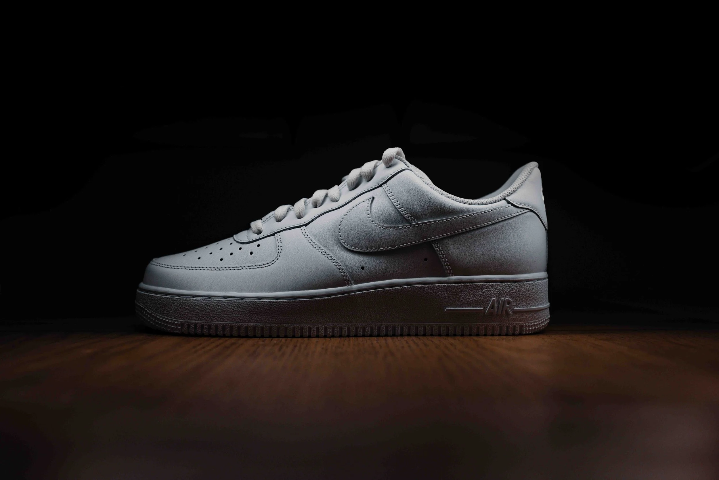 A white Nike Air Force 1 sneaker on a wooden surface with a dark background