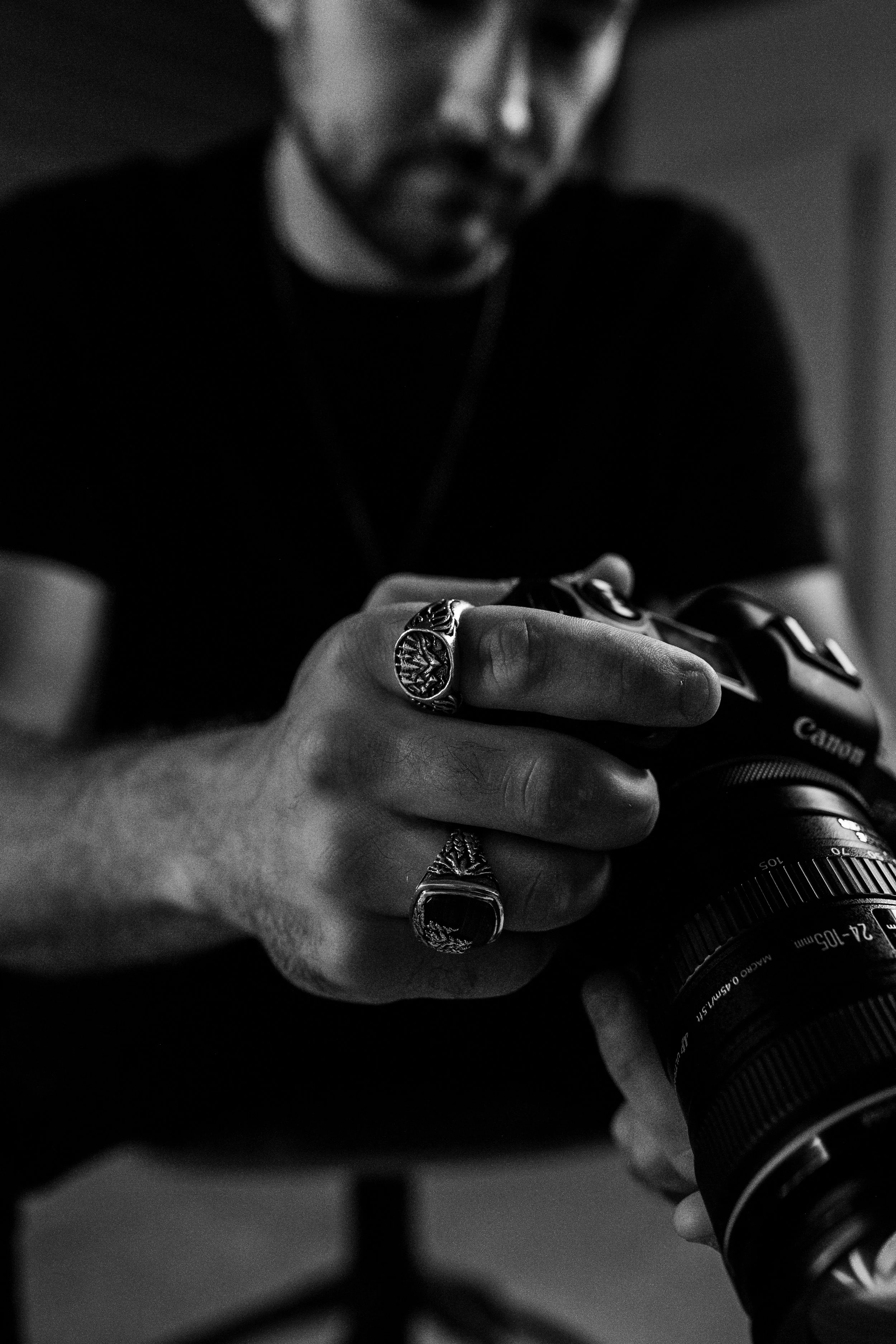 Close-up of a person using a digital camera, focusing on their hand with rings, with a blurred face in the background.
