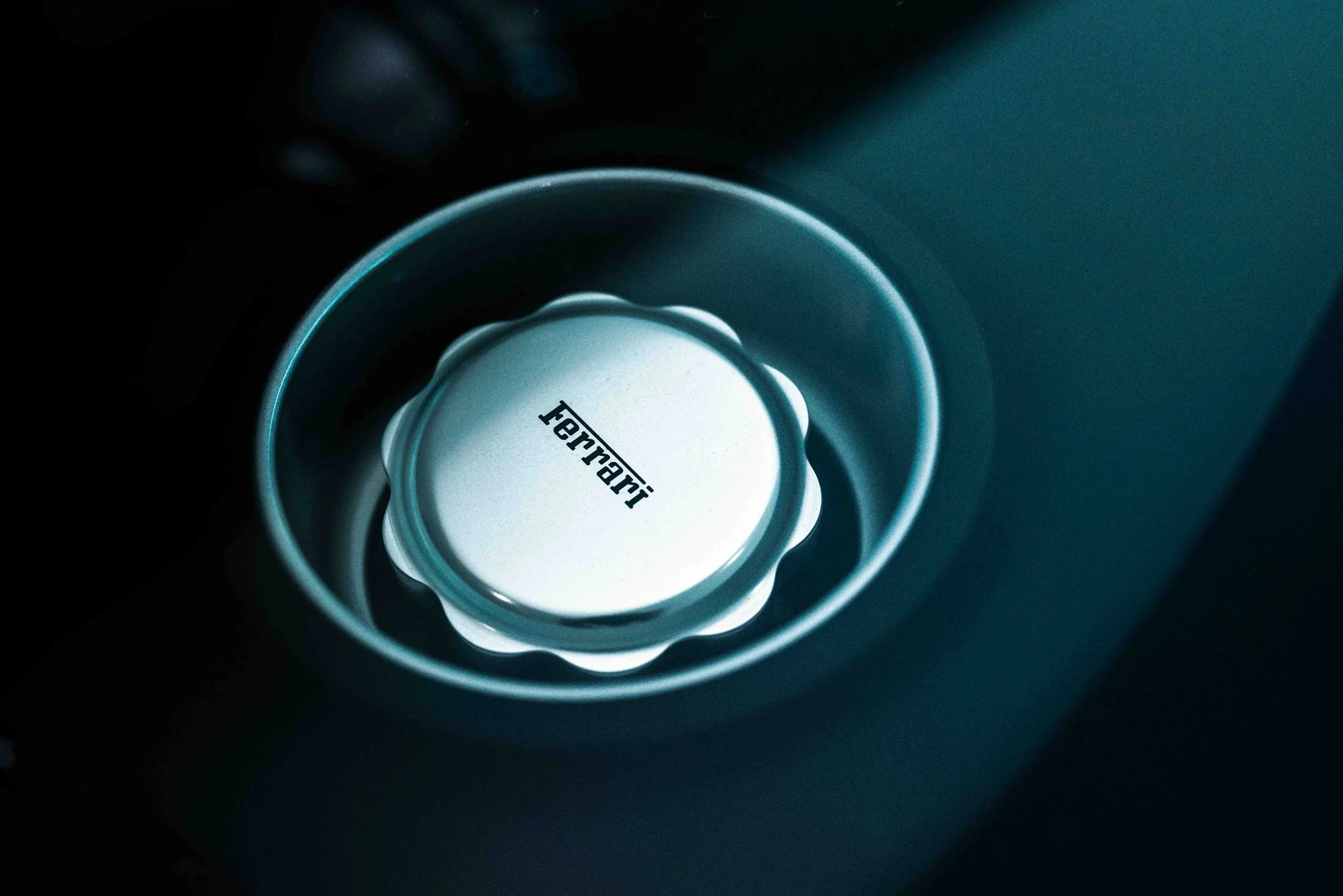Close-up of a Ferrari car's dial or control knob with a metallic finish, embedded in a dark dashboard.