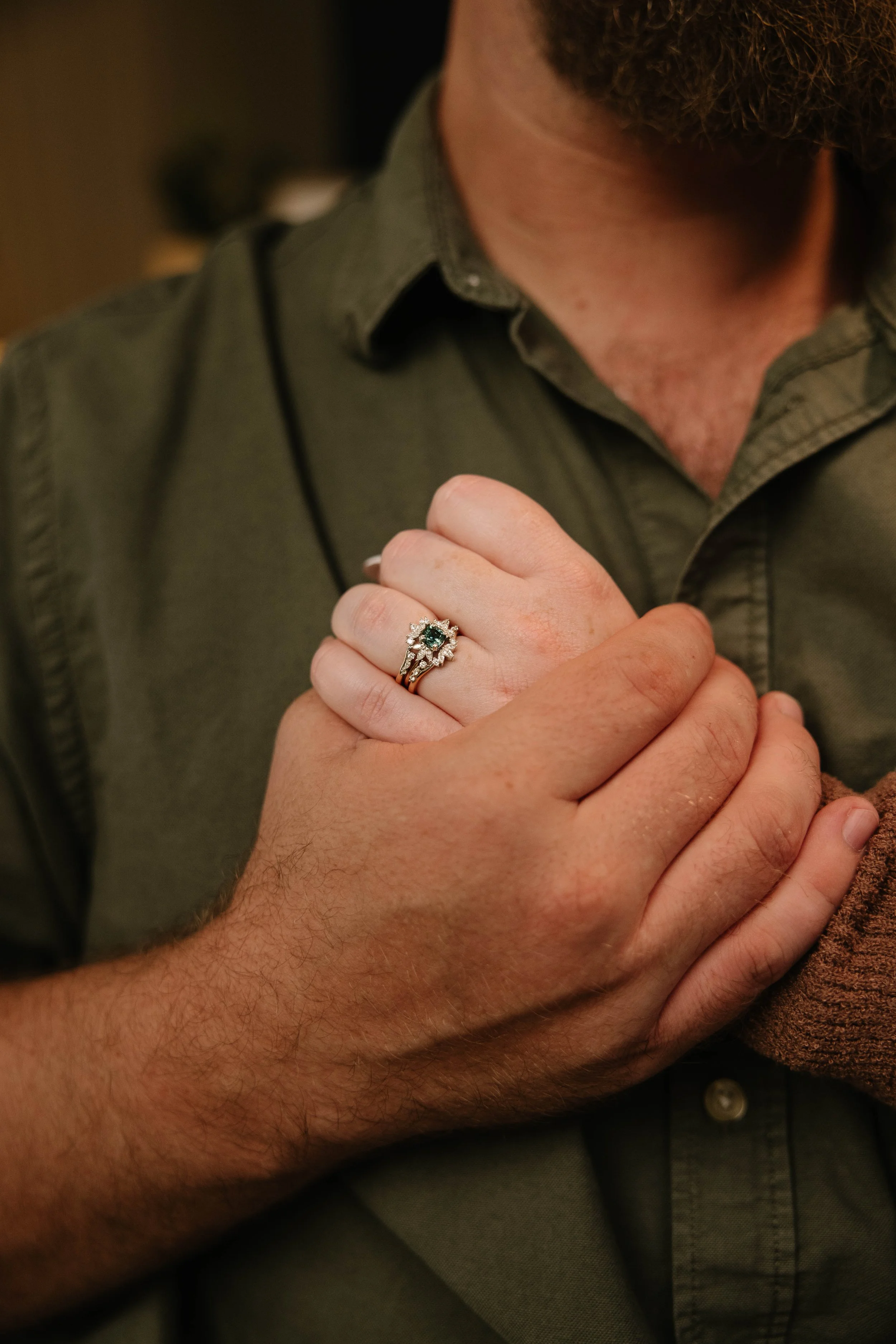A man wearing a green shirt is holding his hand over his chest, showing a ring on his finger.