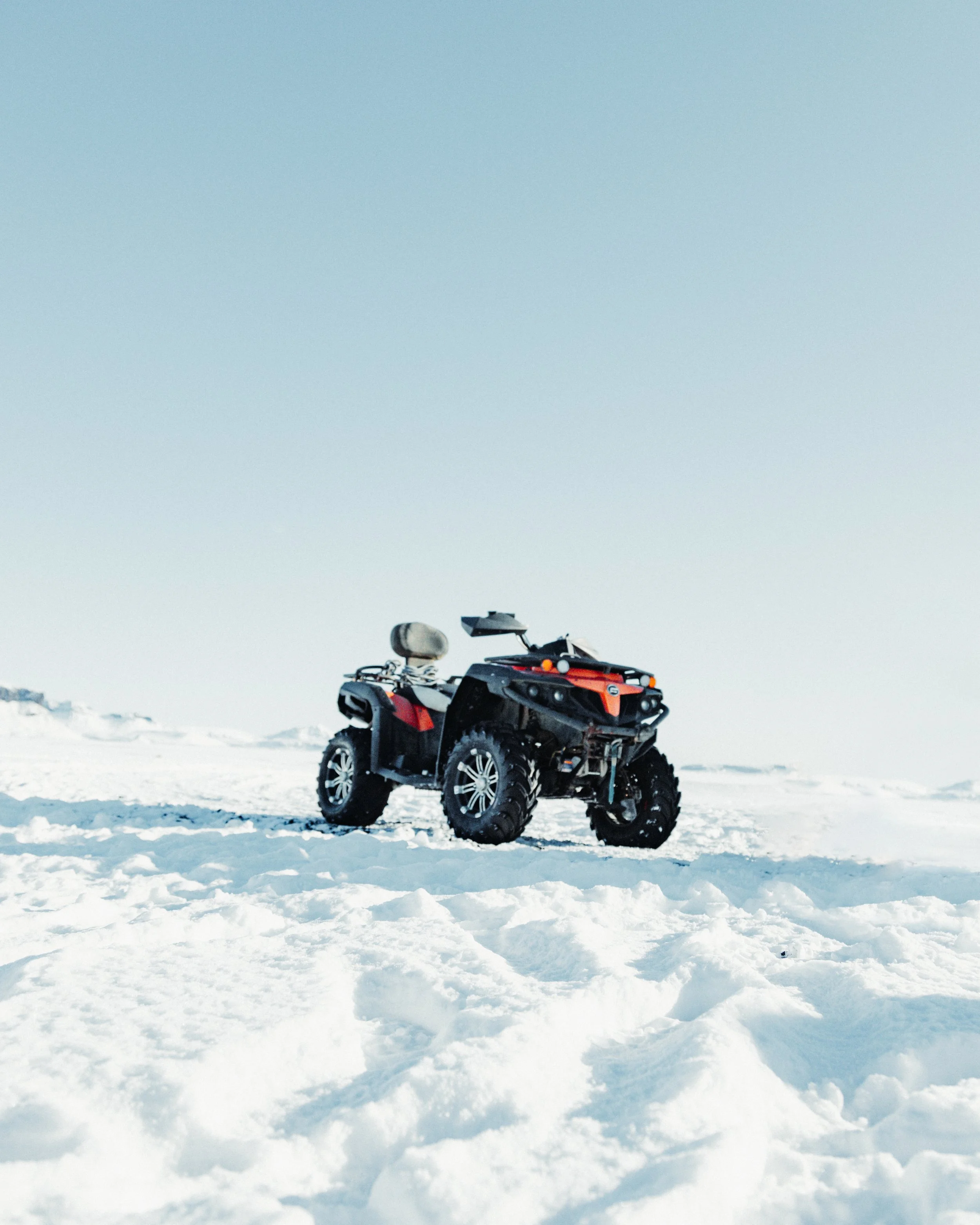 A black and orange all-terrain vehicle (ATV) parked on snow-covered ground under a clear sky.