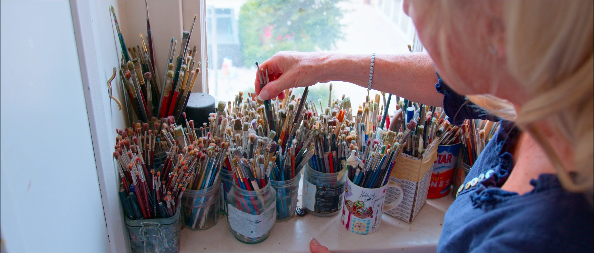 Woman organizing paintbrushes in containers on a windowsill.