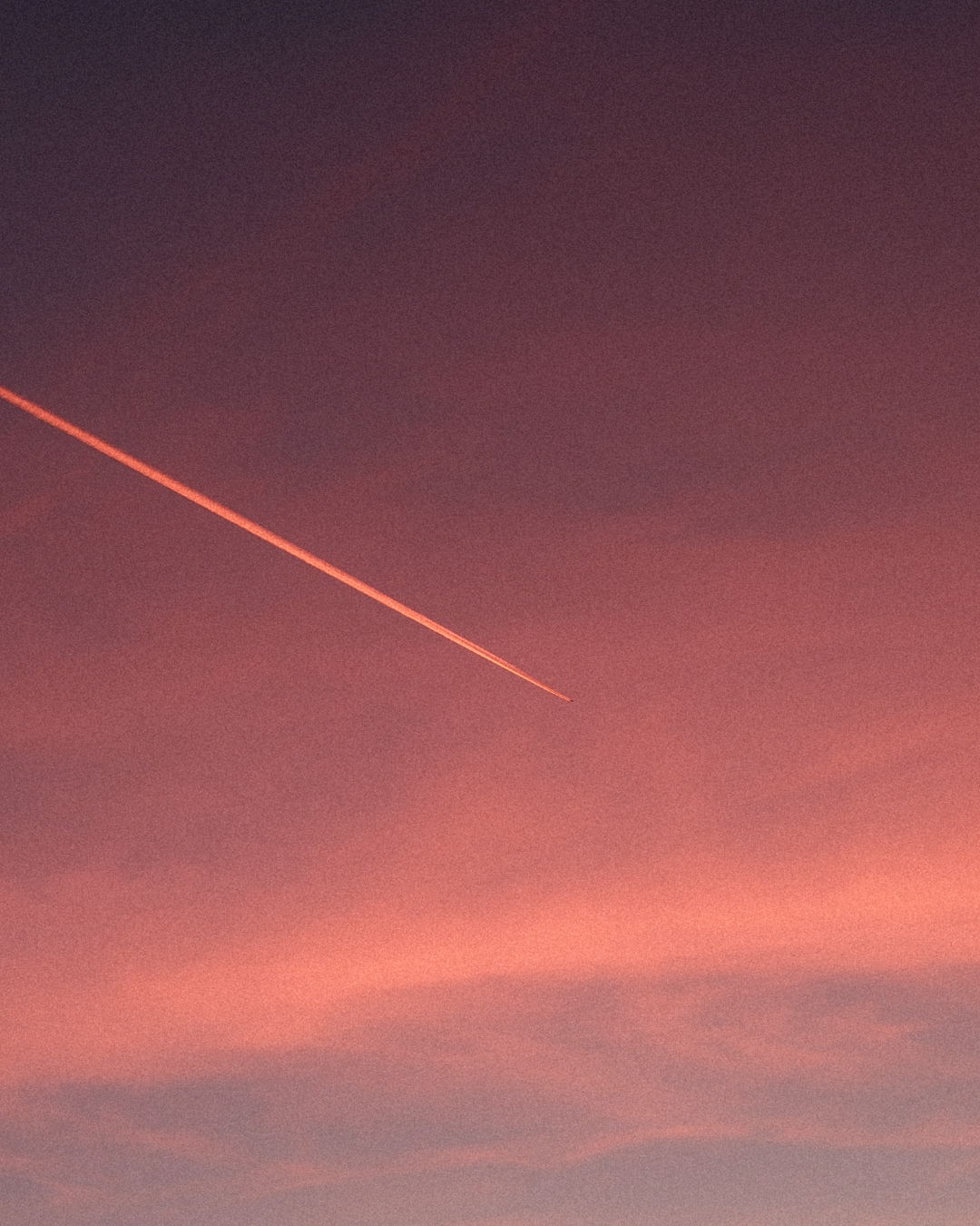 Pink and purple sky during sunset with a visible airplane contrail.