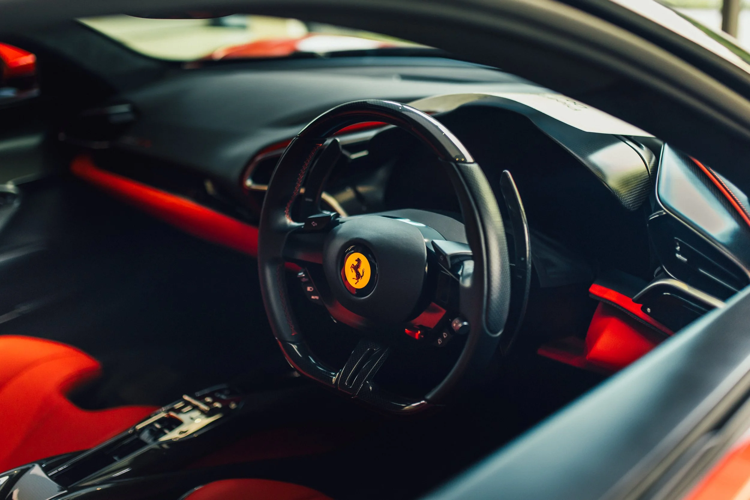 Close-up of the interior of a Ferrari sports car, featuring a steering wheel with the Ferrari logo, and a black and red dashboard.