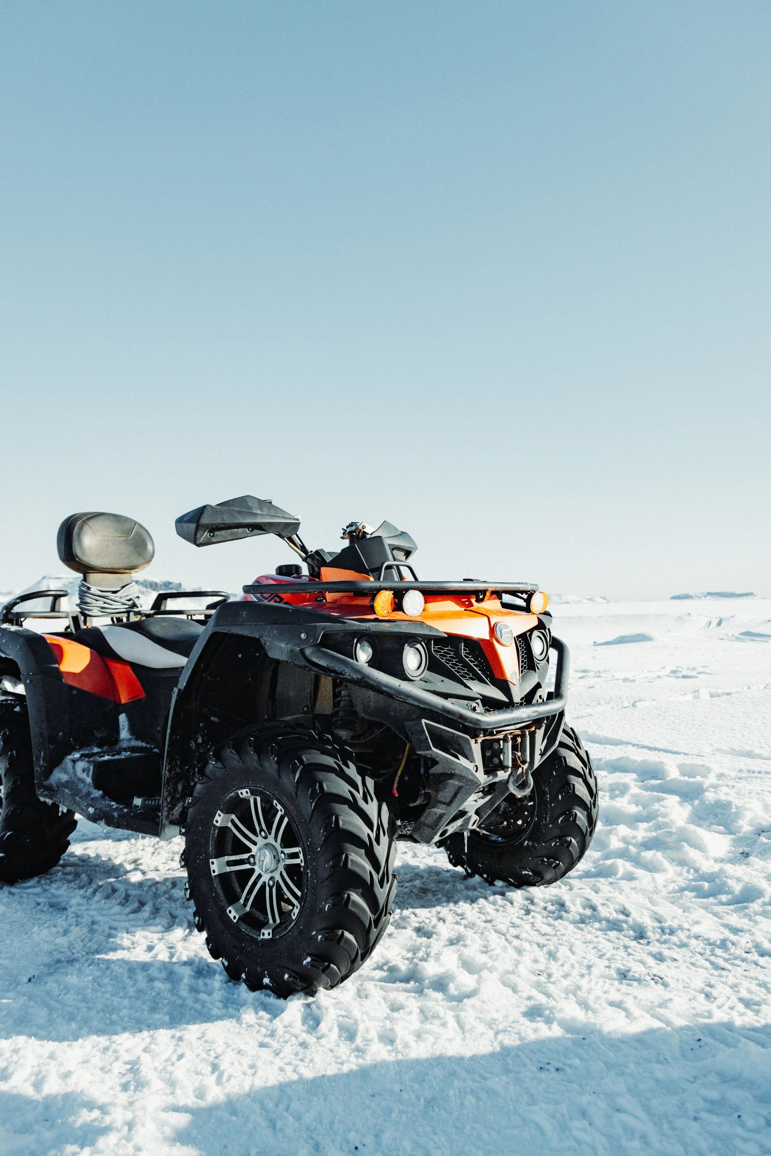 Orange and black all-terrain vehicle (ATV) on snow-covered landscape under clear blue sky.