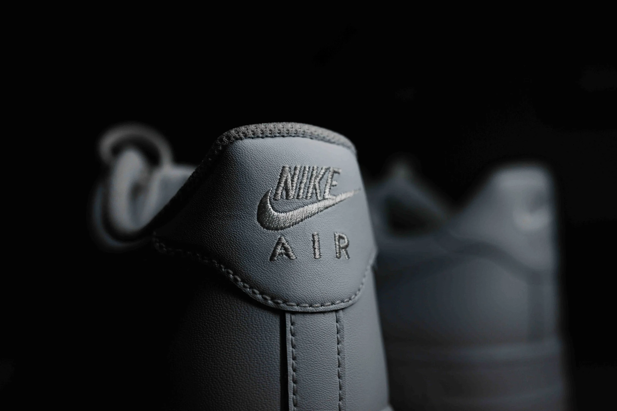 Close-up of a gray Nike Air sneaker with detailed stitching and logo, against a black background.