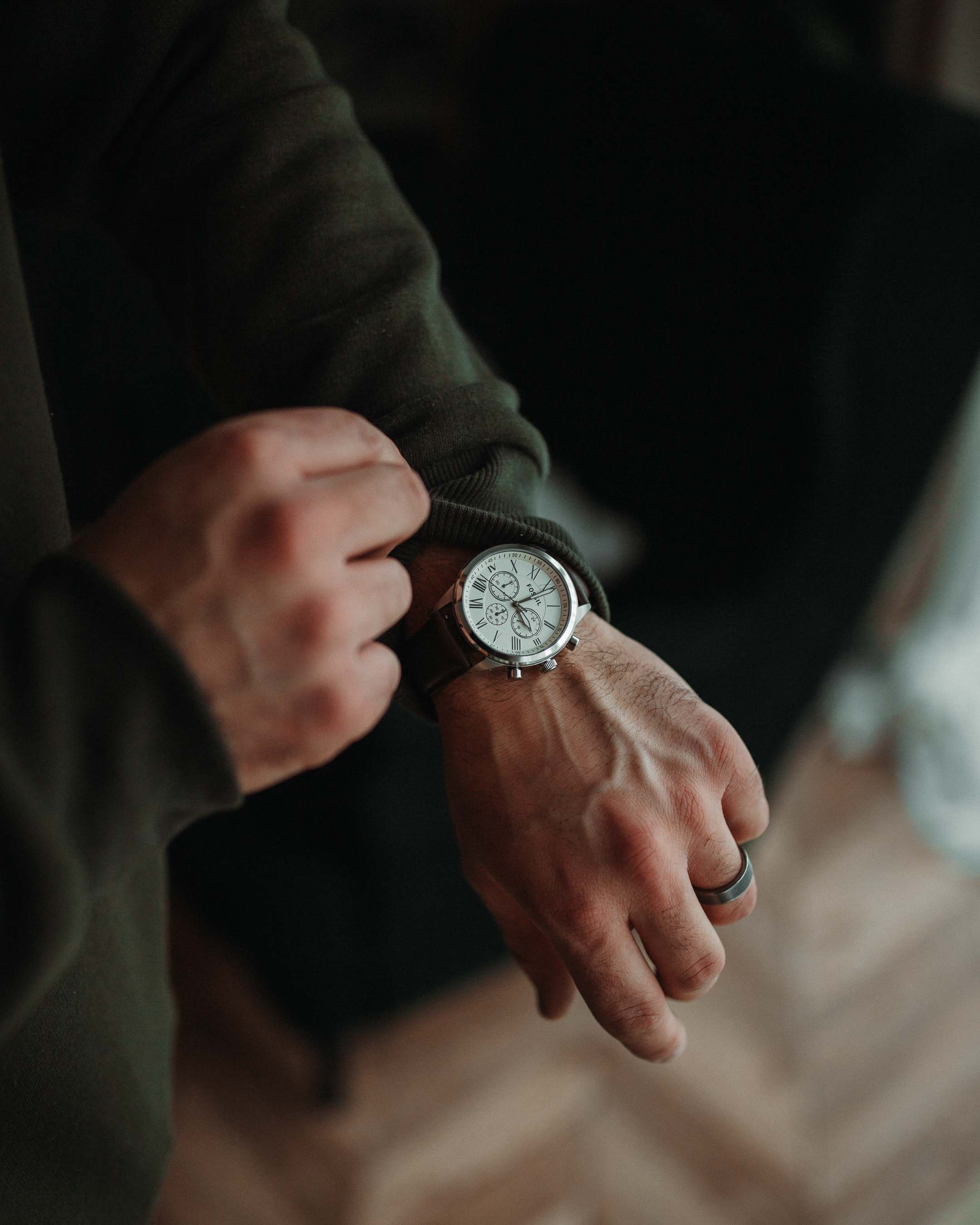 A person wearing a dark long-sleeve shirt looking at their wristwatch with a leather strap.