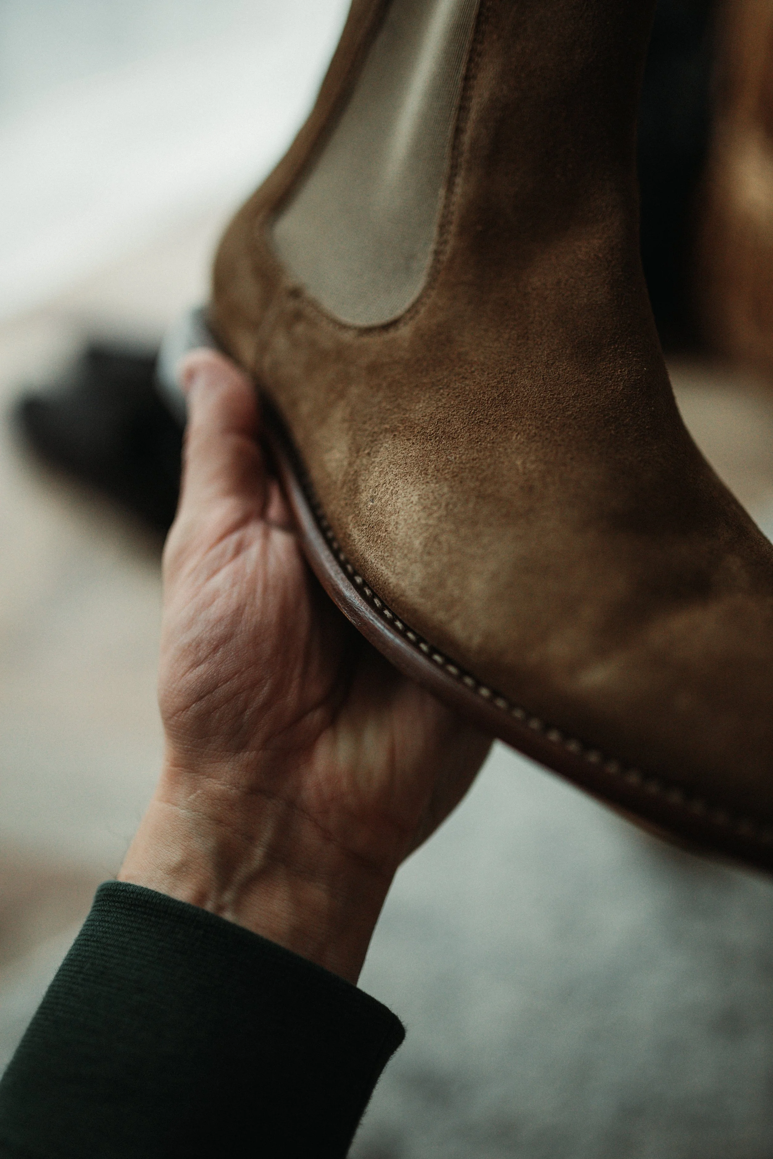 Close-up of a hand holding a brown suede ankle boot with a zipper.