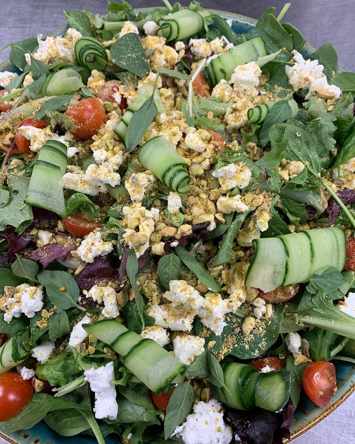 Salad with cherry tomatoes, cucumber ribbons, crumbled cheese, chopped hard-boiled eggs, and greens in a bowl.