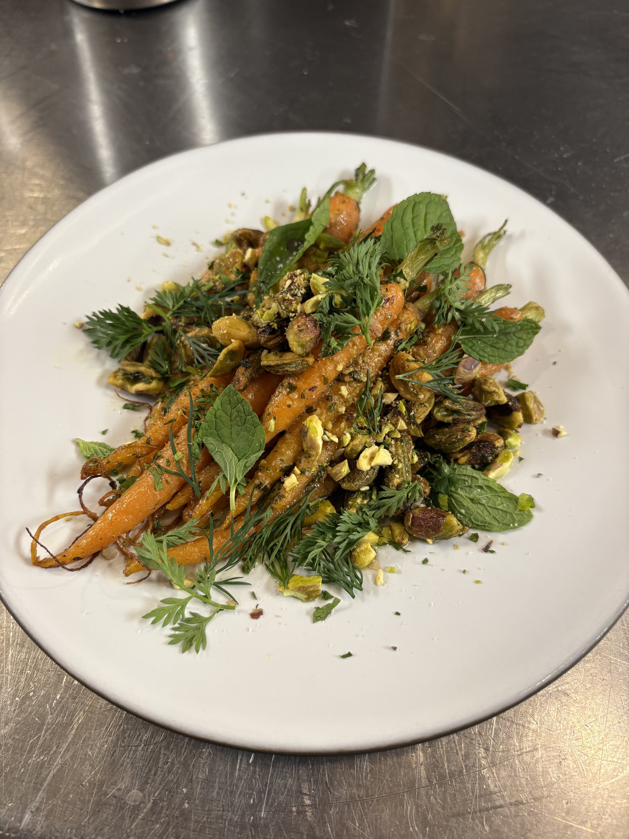 A plate of roasted carrots and green beans garnished with fresh herbs and chopped pistach nuts.