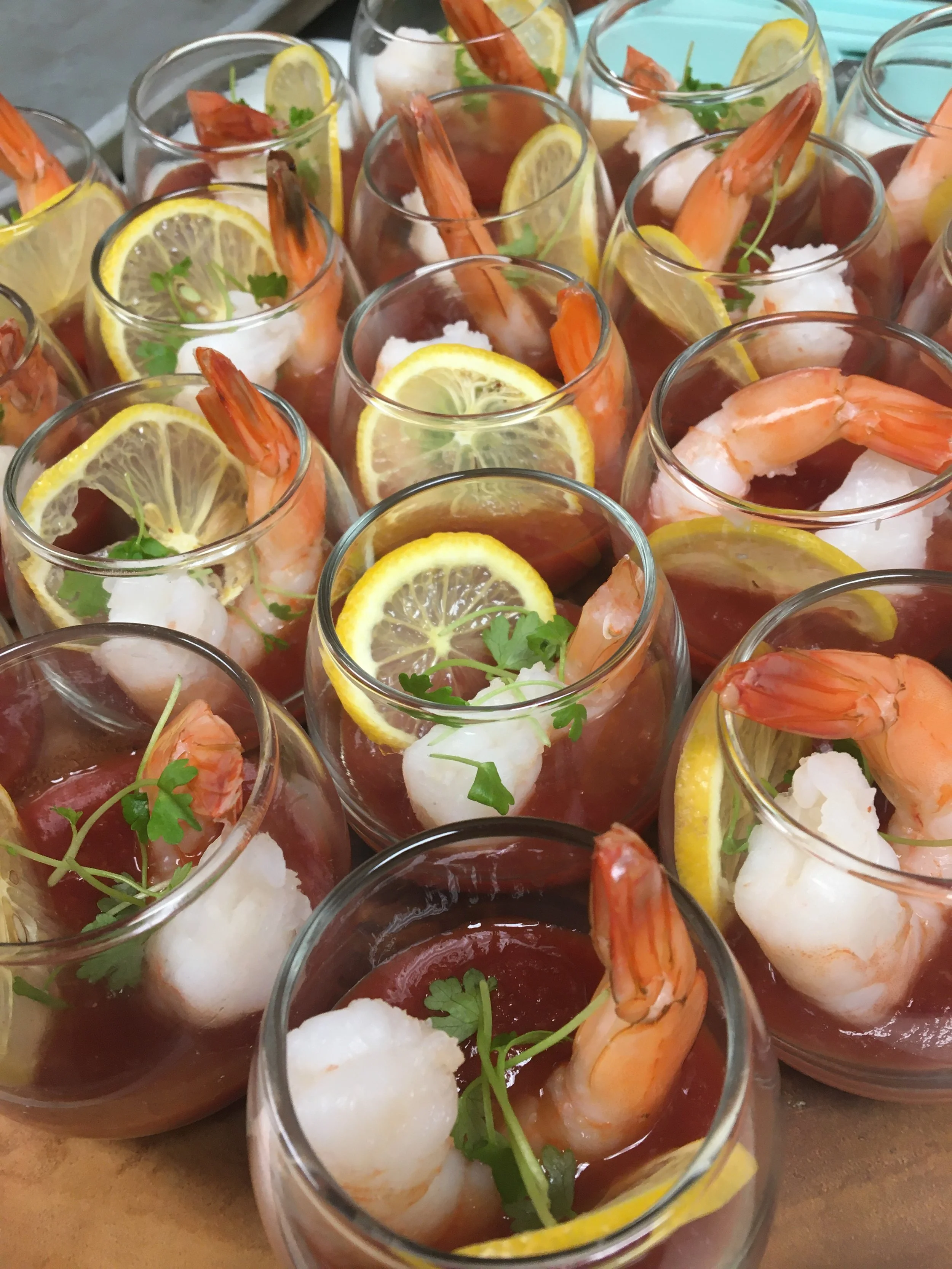 Multiple glasses of shrimp cocktail garnished with lemon slices, fresh herbs, and a dollop of sauce.