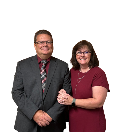 A man and woman dressed in formal attire standing together, smiling, with the woman holding the man's arm.