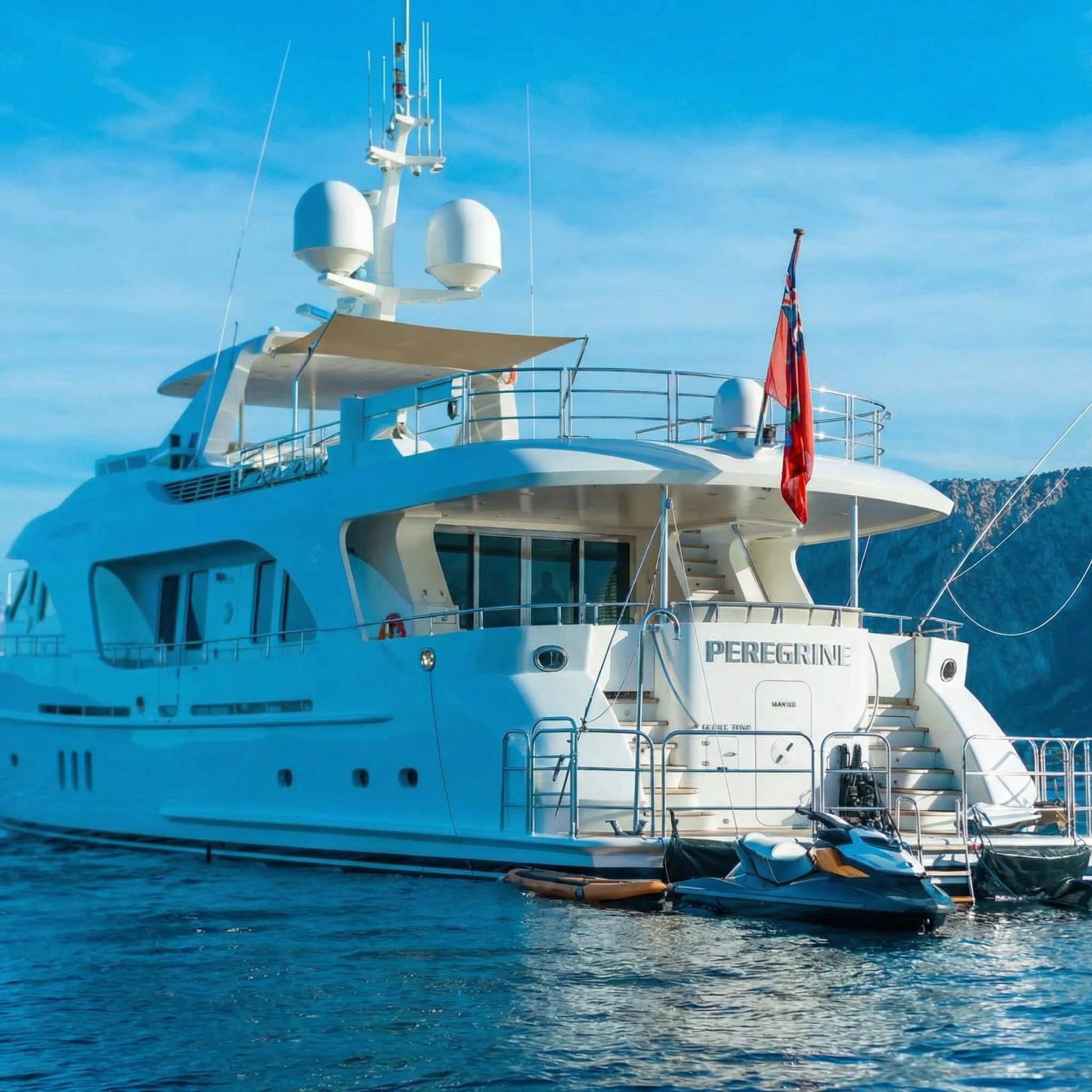 A luxury white yacht named Peregrine docked on calm blue water with a mountain in the background, displaying antennas, radar, and equipment on deck.