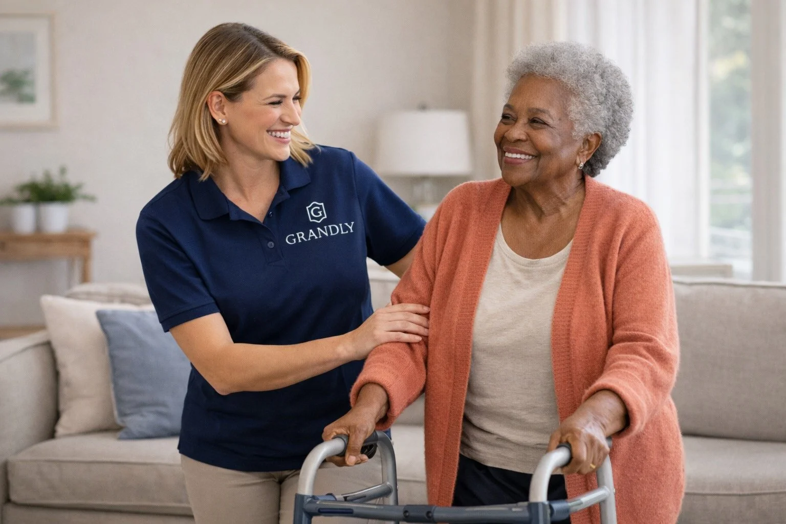 A caregiver assisting an elderly woman with a walker in a living room, both smiling.