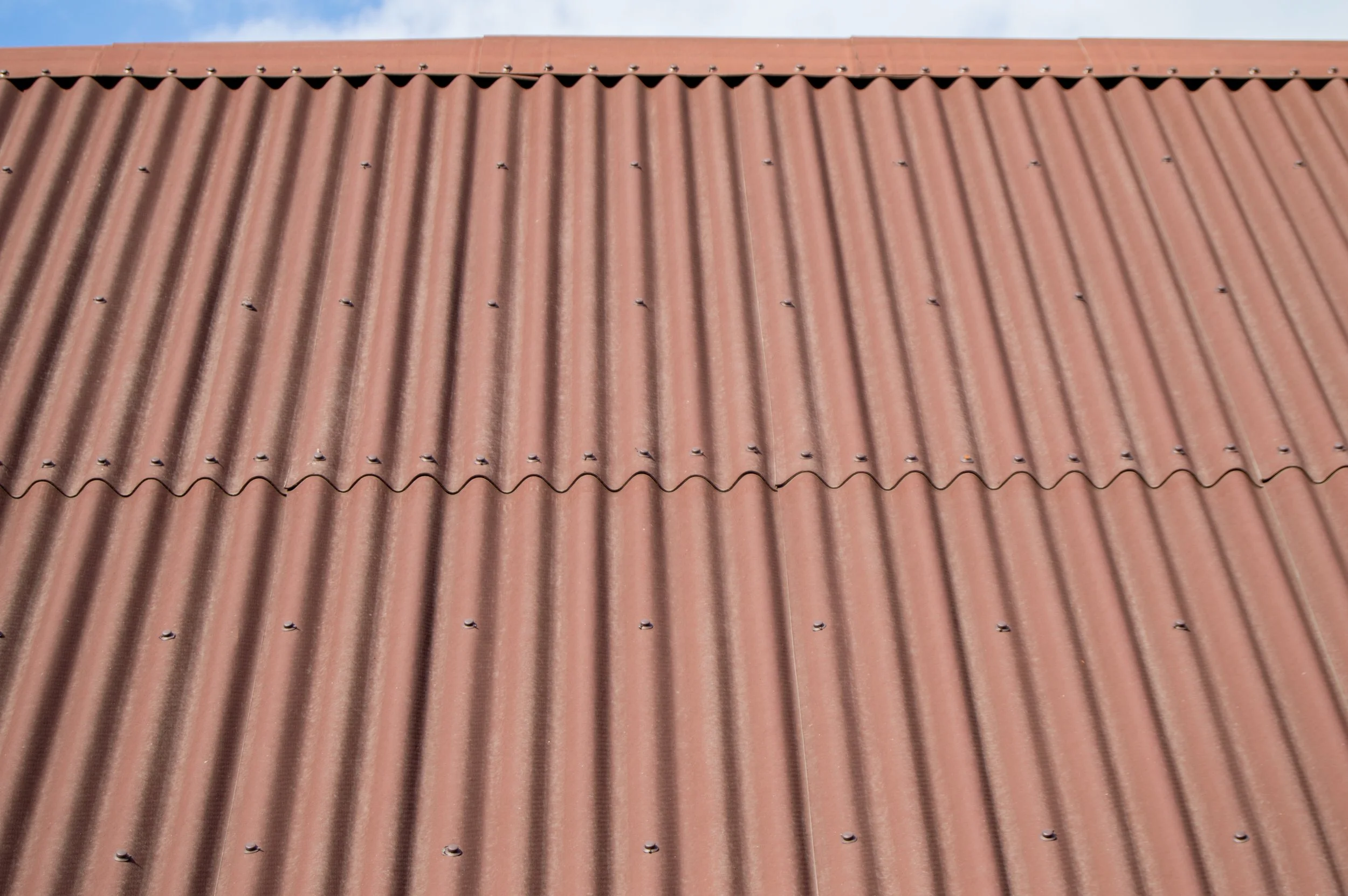 Close-up of a corrugated metal roof with a reddish-brown color and evenly spaced screws.