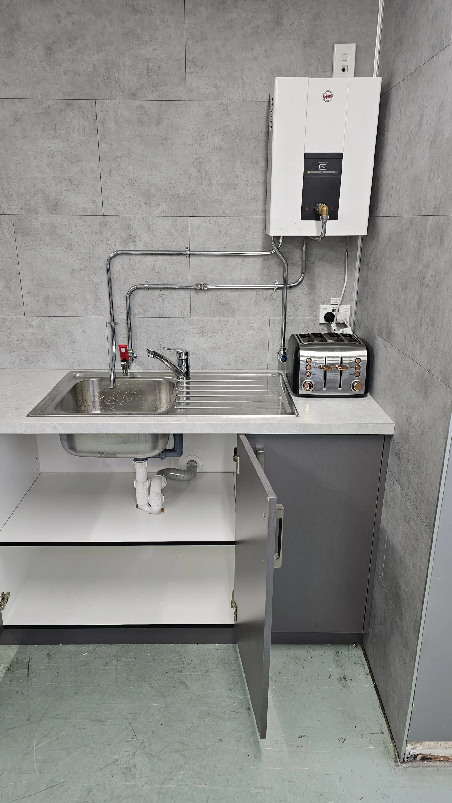 Small kitchen sink with a drying rack, toaster, water heater, and plumbing underneath