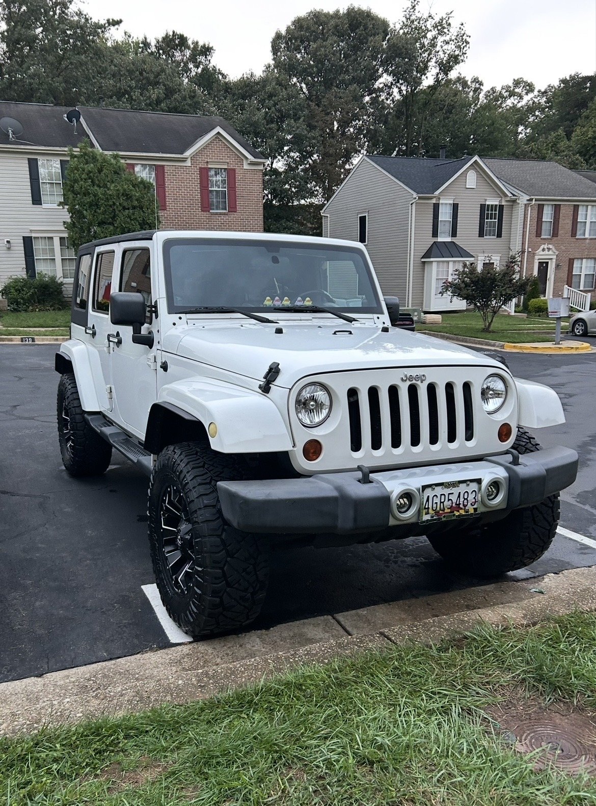 A white Jeep SUV parked in a residential parking lot with houses and trees in the background.