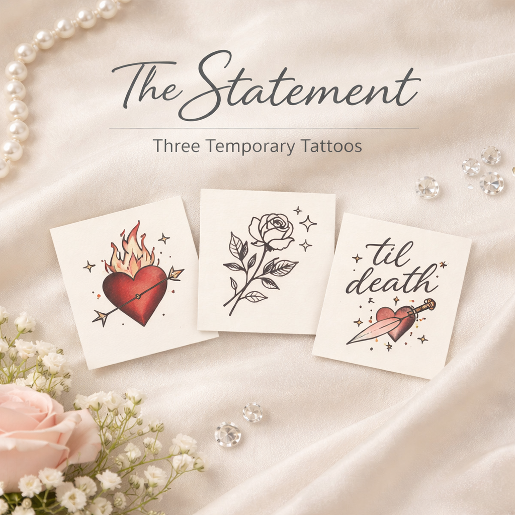 Three temporary tattoo designs on small cards with floral and heart themes. One shows a flaming heart with an arrow, the second is a rose, and the third says 'til death' with a heart and dagger. The background is satin with pearls, flowers, and rhine