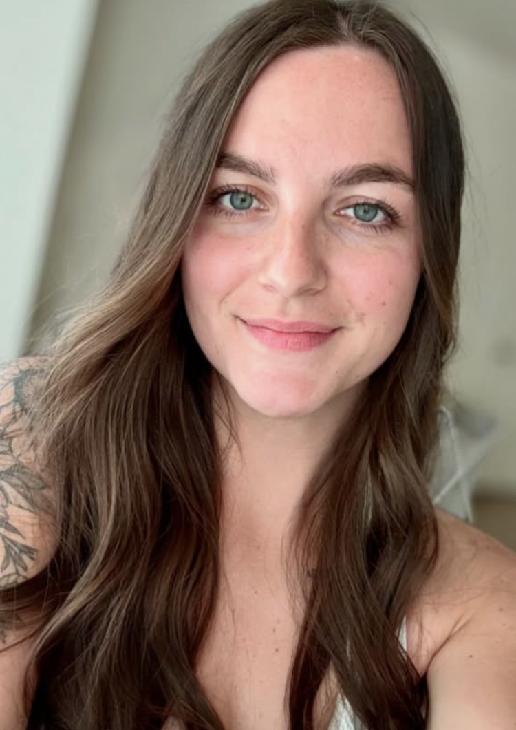 A young woman with long brown hair and blue eyes, smiling at the camera.