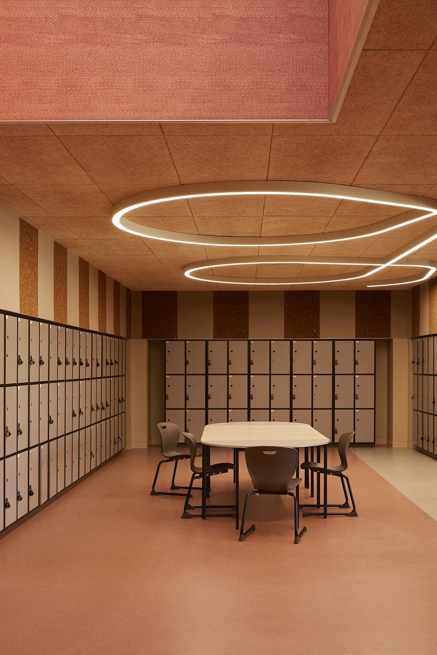 The student locker room at Auburn High school features a textural cork ceiling and sculptural ceiling light, terracotta toned printed acoustic panelling and a communal table and chairs - which create a warm and modern space for students to hang out.