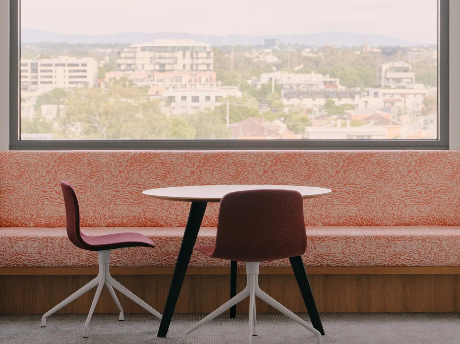 A breakout area within Melbourne Indigenous Transition School featuring banquet seating in printed upholstery fabric beneath a large window with expansive views over Richmond and surrounds.