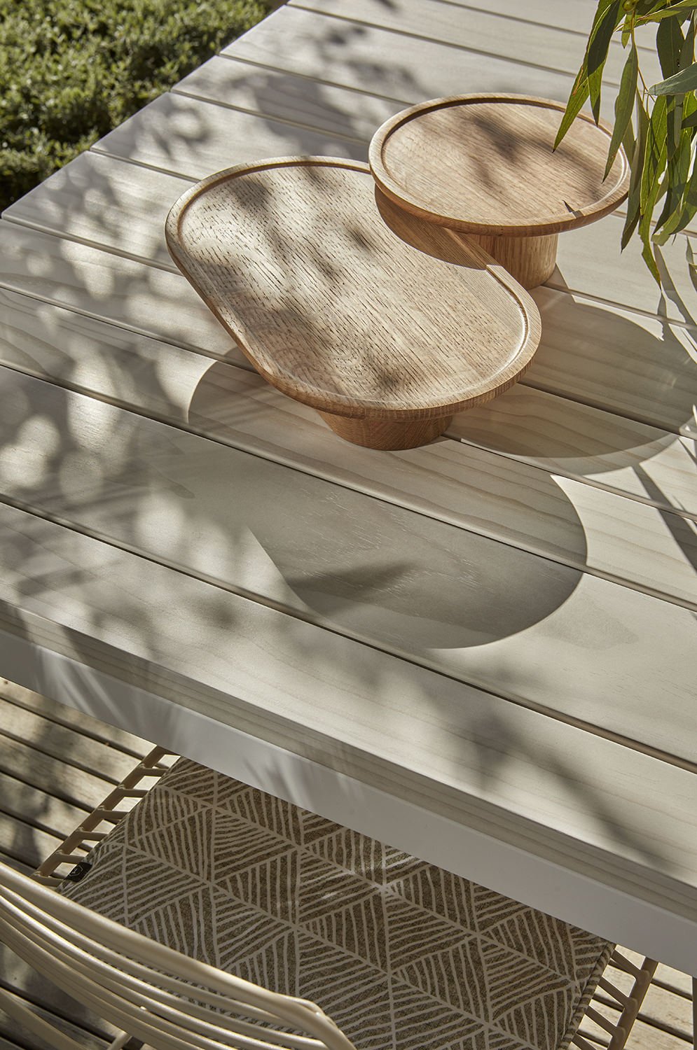 Outdoor table setting with timber trays and a potted plant, and green patterned seat cushion visible on the bench seat below.