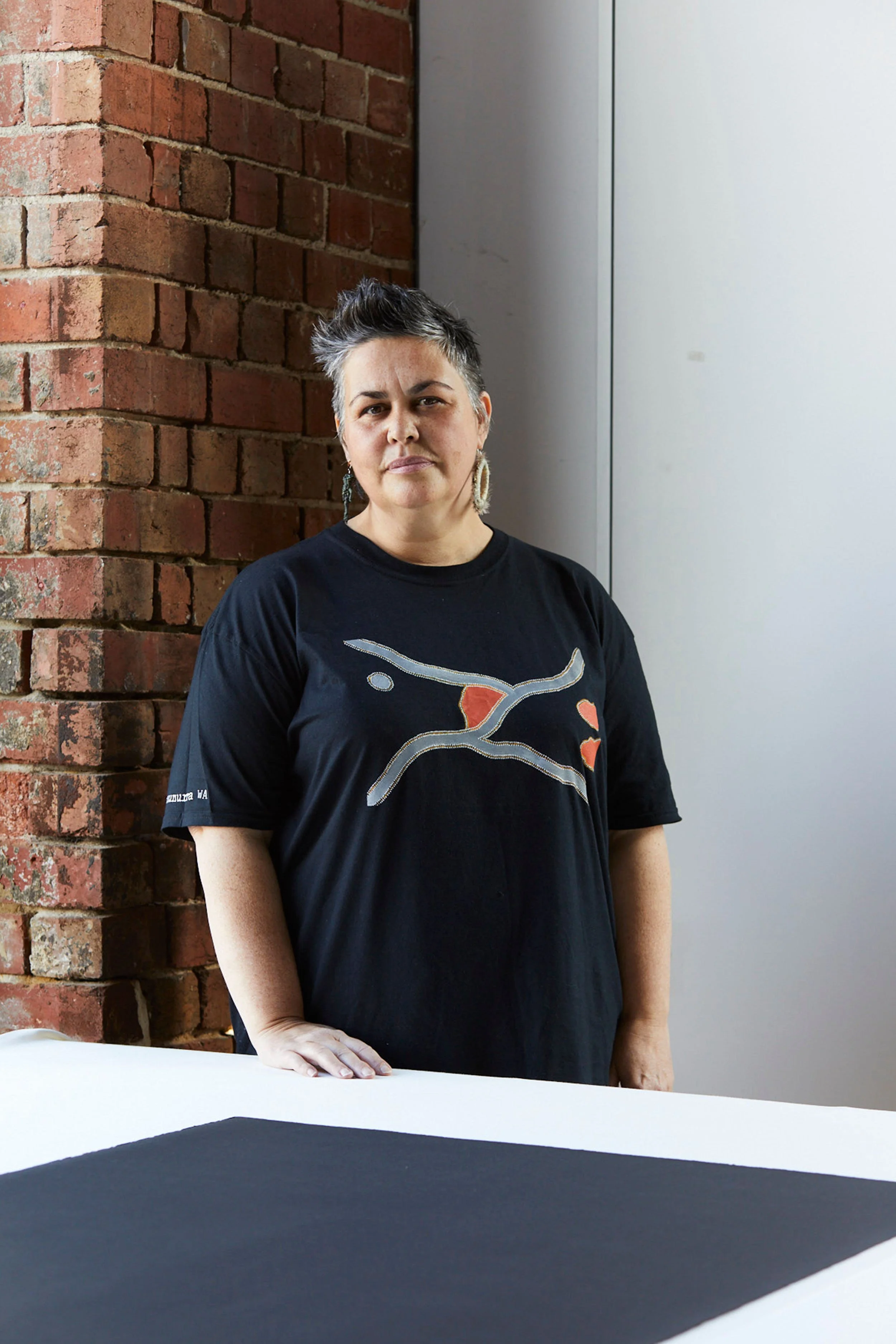 A colour portrait of an Indigenous woman with a brick wall in background.
