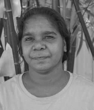 Black and white portrait of Indigenous woman, with plants in the background.