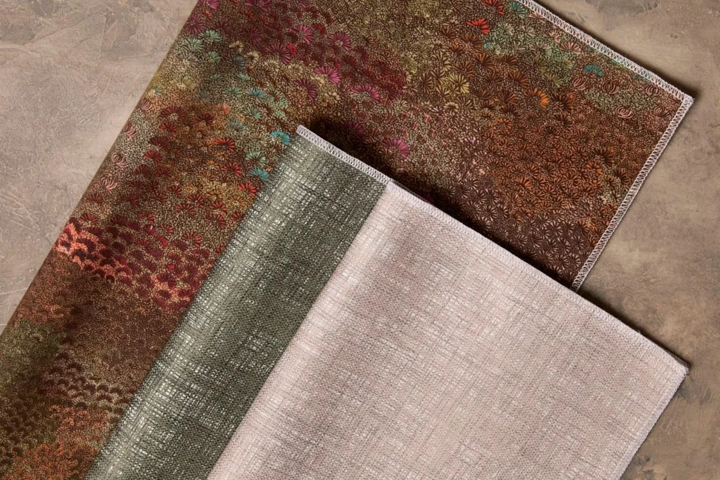 Three fabric pieces arranged on a flat surface, in silver, green and rich red colours.