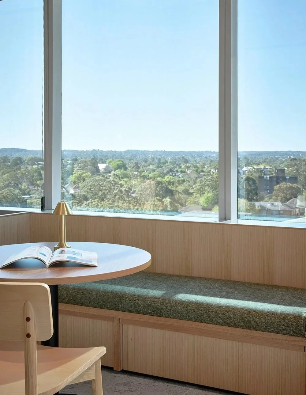 Banquette seat in modern office with window overlooking trees below and blue sky, featuring green First Nations design on upholstery with wooden table, chair and joinery