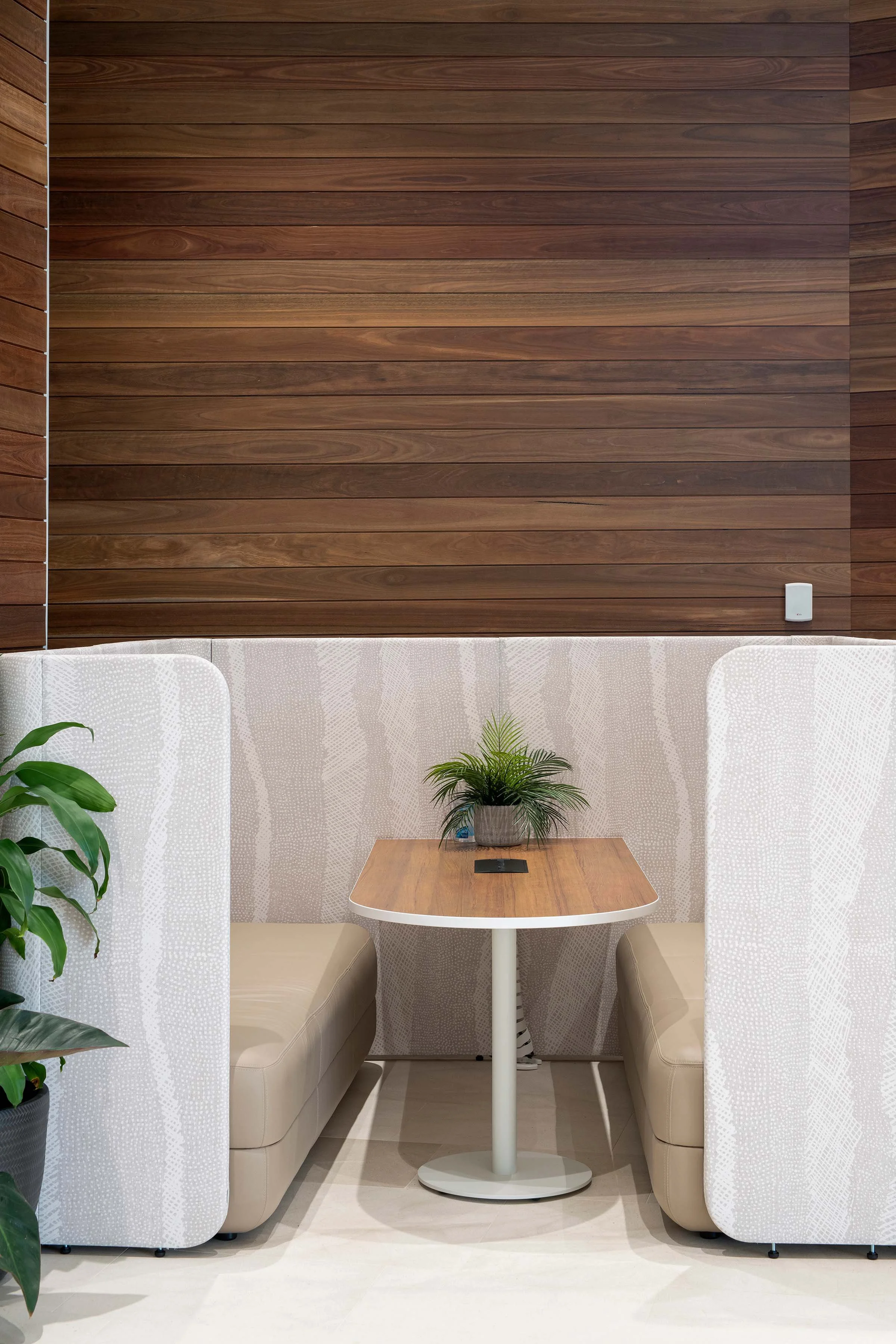 Booth seating in the new Ipswich City Council building. The booths are upholstered with a stone and cream coloured patterned fabric. The pattern includes cross hatching and dots. The walls around the booths are dark timber panelling